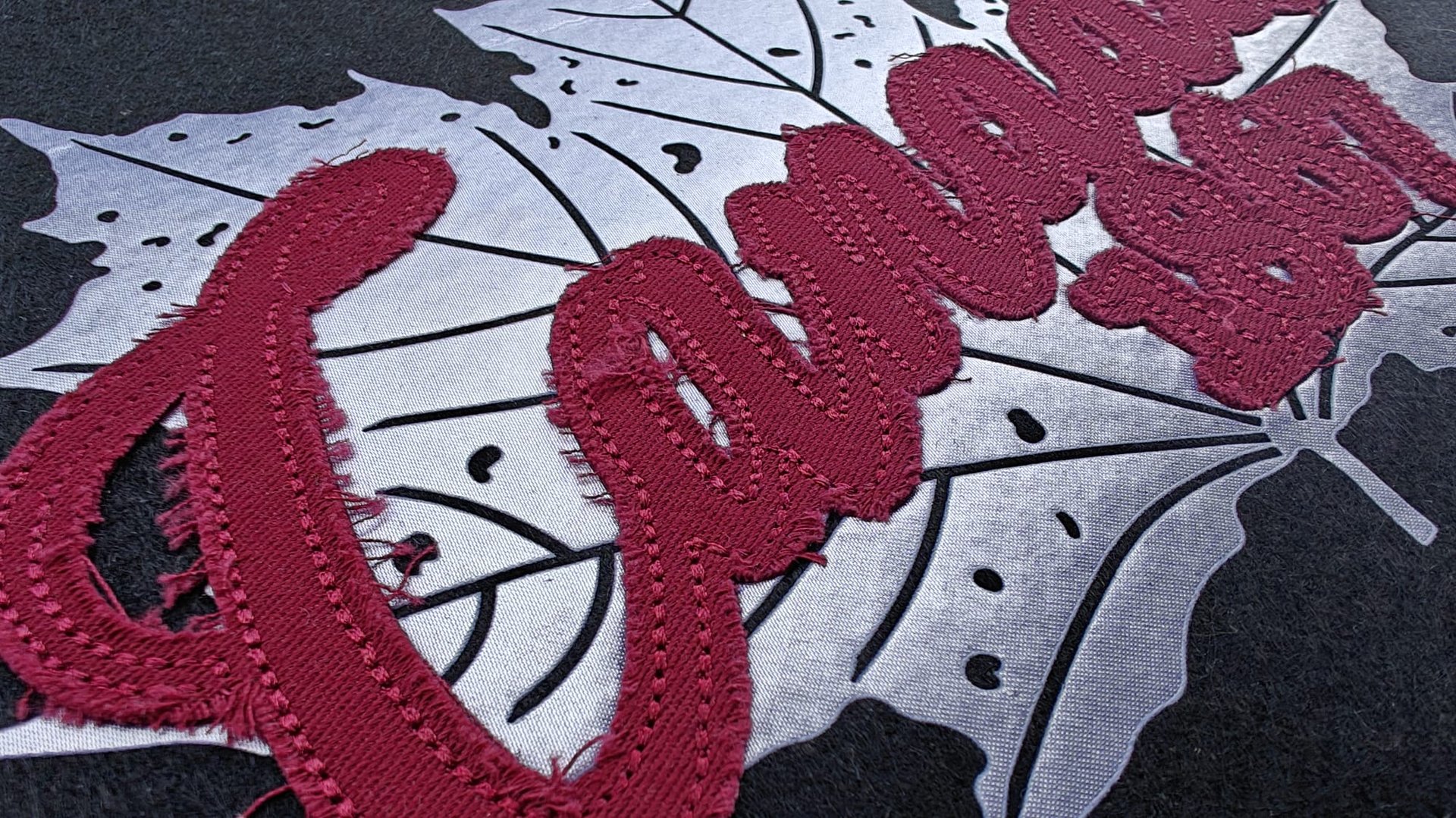 Close-up of embroidered red script Canada 150 on a stylized maple leaf background on a dark fabric.