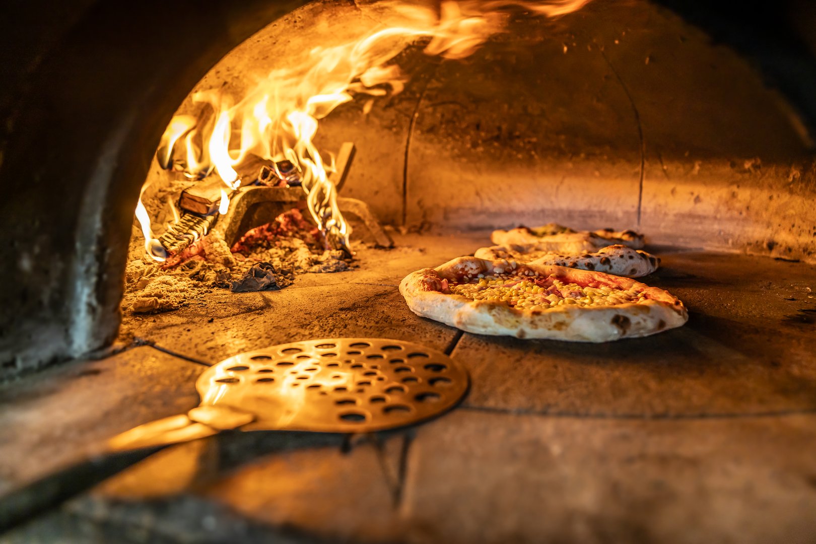 Traditional oven for baking pizza with burning wood and shovel. The cook rotates the pizza in the oven to ensure even baking.