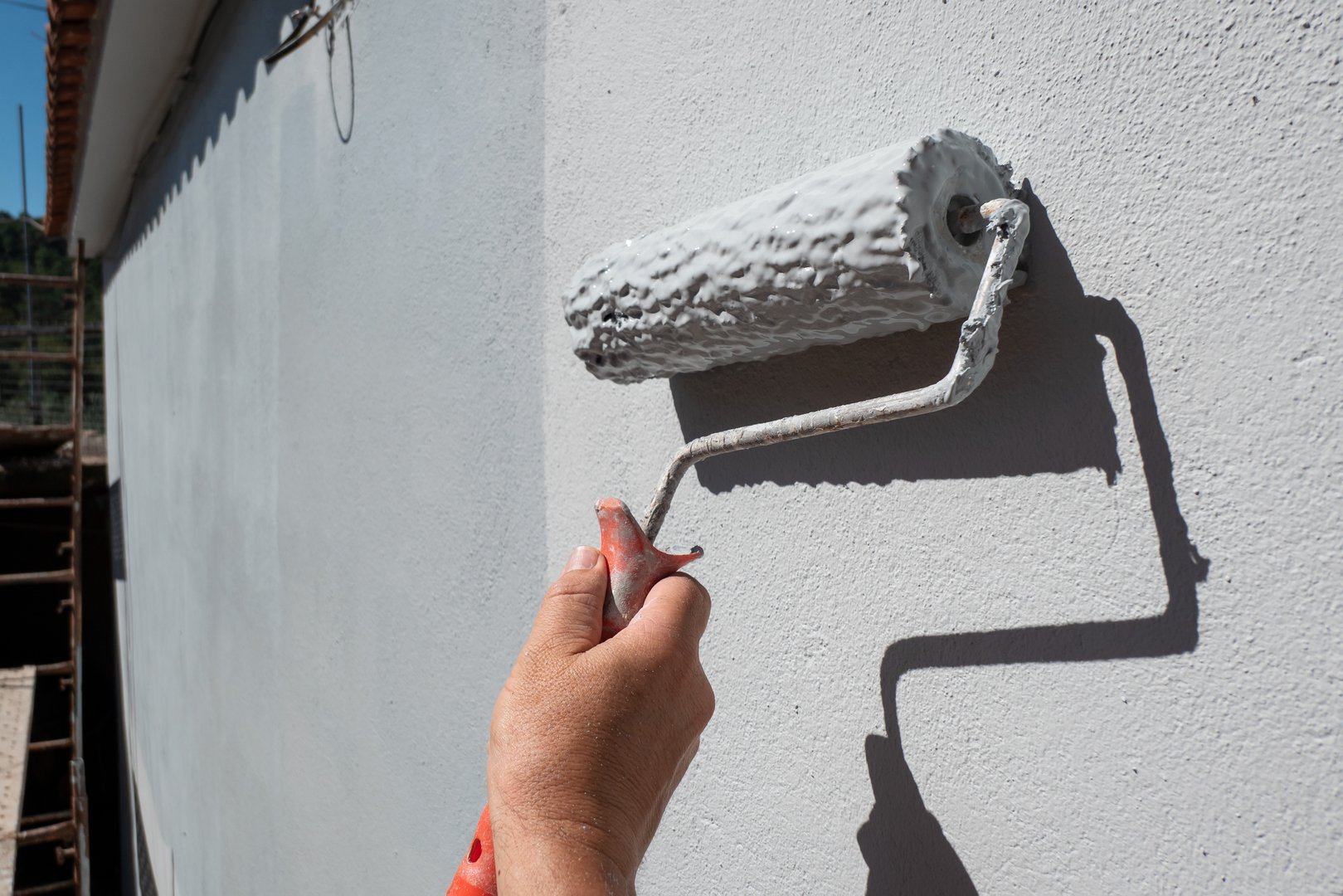 Painter's hand holding a roller filled with paint to paint an exterior wall