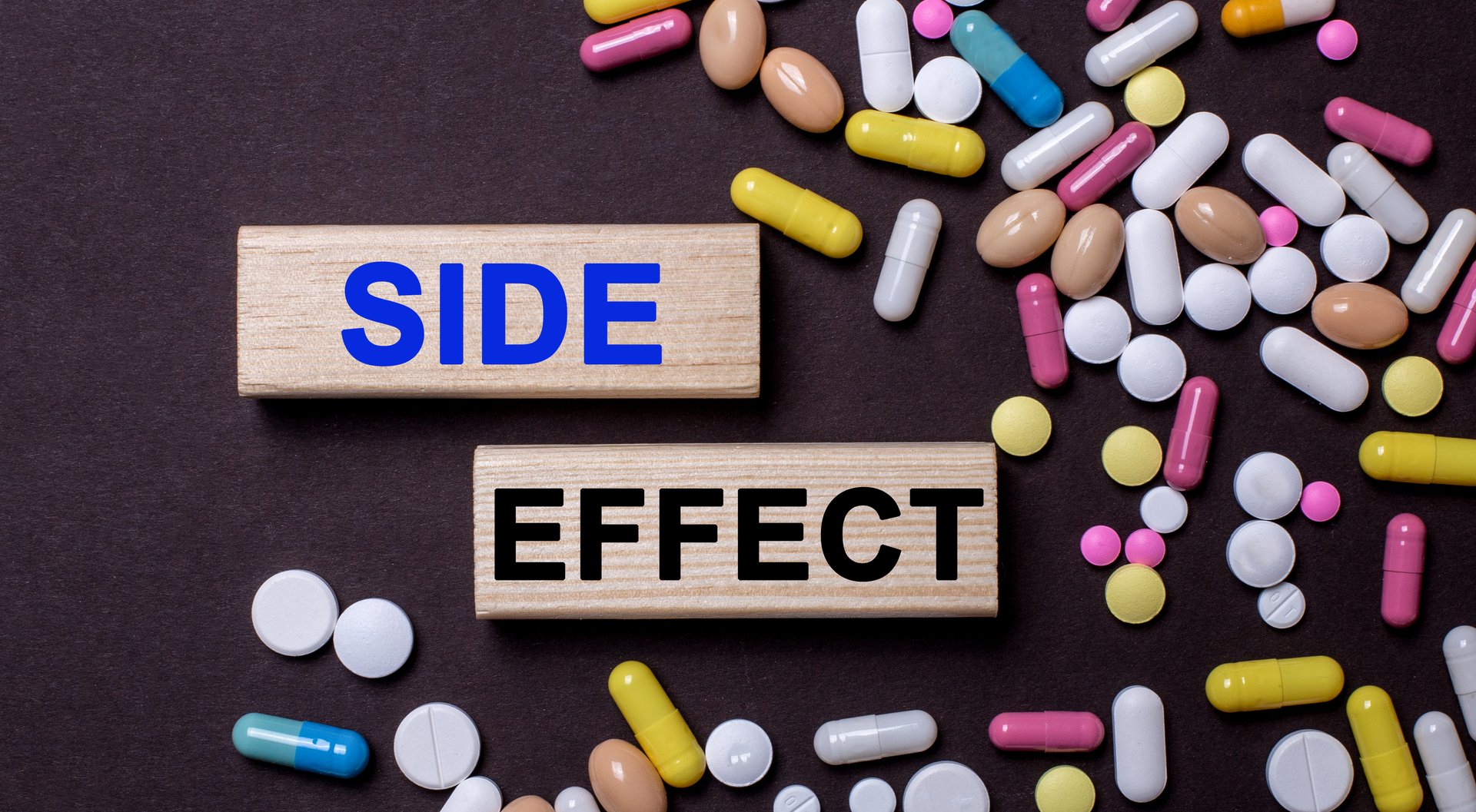 Side effect - words on wooden printed blocks between multi-colored tablets on a dark background