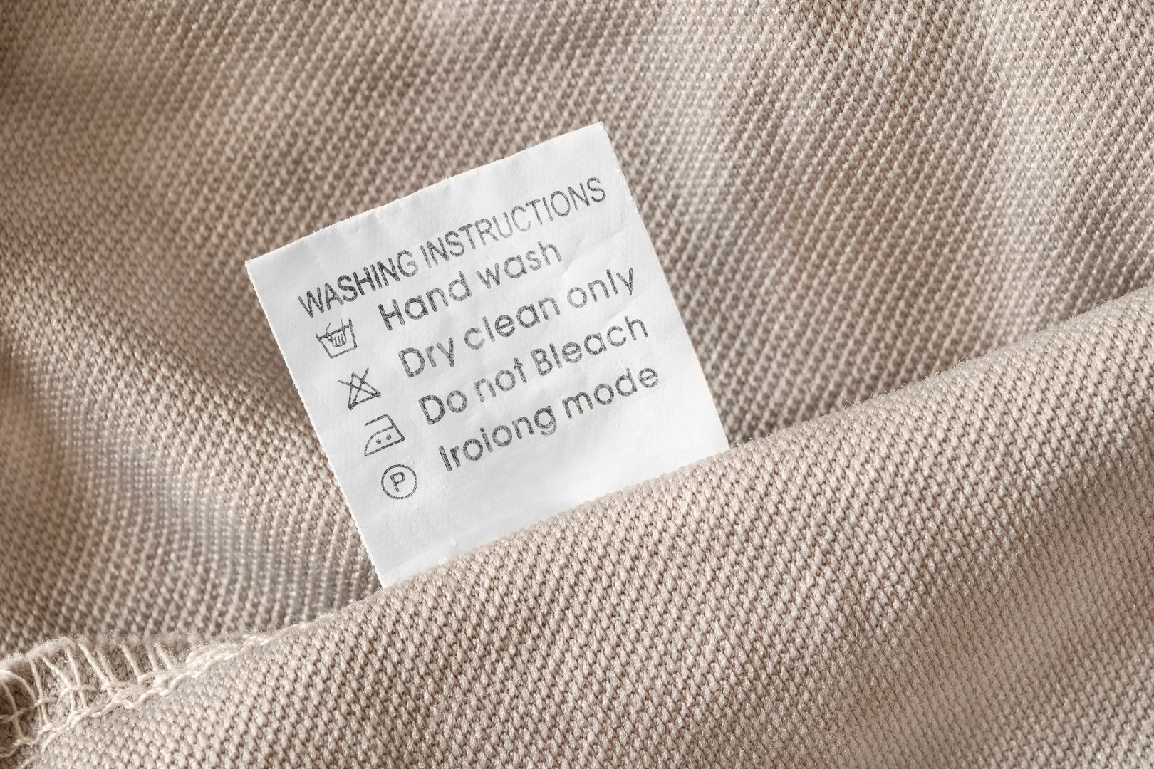 Washing instructions clothes label on beige fabric background closeup