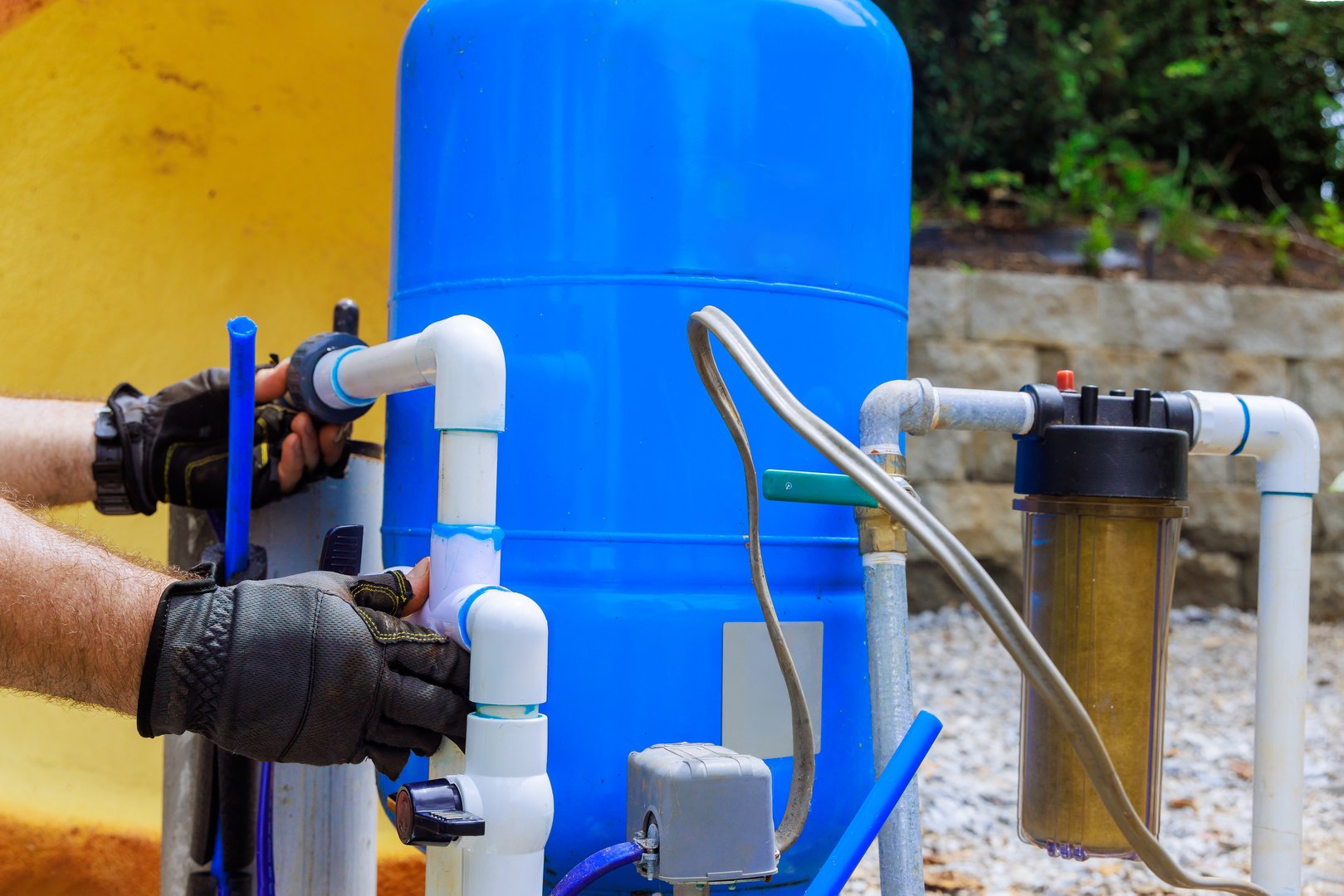 Plumber connects pipes to artesian water well filtration tank during an installation process in backyard.