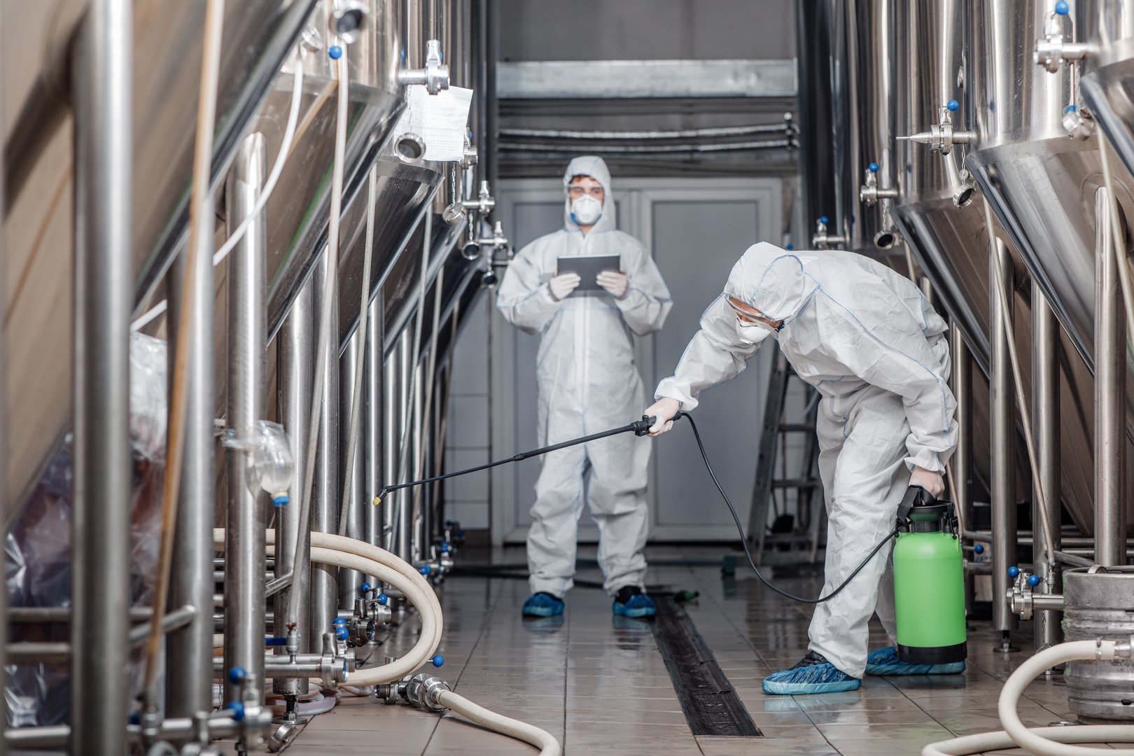 Product quality, factory cleanliness and disinfection. Men in hazmat suits work with spray bags in beer factory, free space