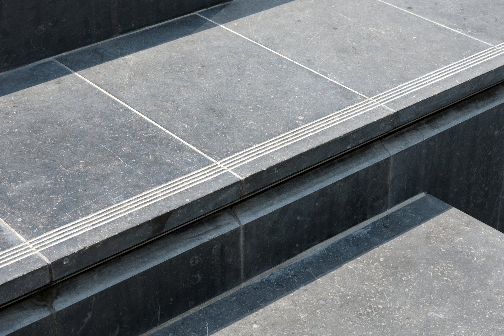 Close-up of a stone step with textured safety grooves on dark blue stone tiles under natural light.