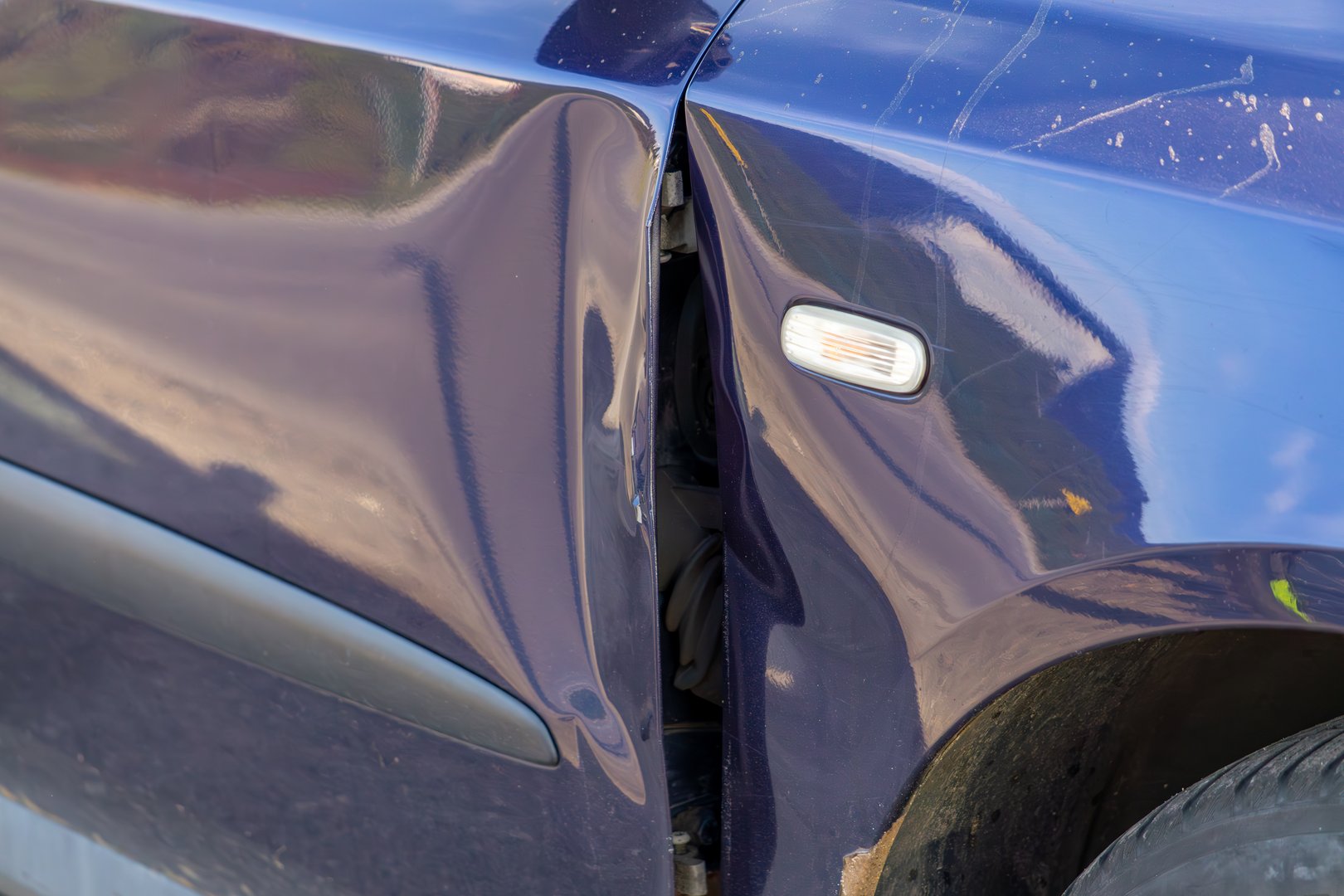 dented metal. dent on car door and front fender from parking collision. vehicle damage