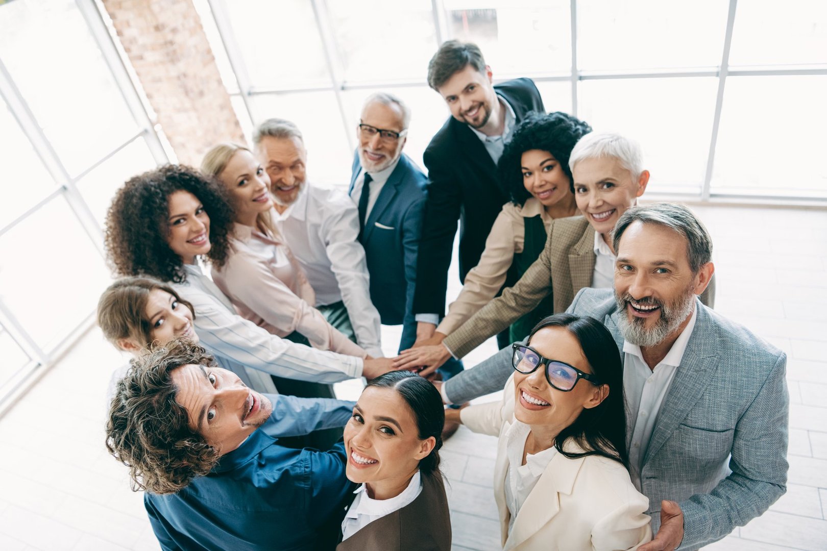 A diverse group of professionals forming a team huddle indoors, symbolizing camaraderie, teamwork, and a collaborative environment in corporate settings.