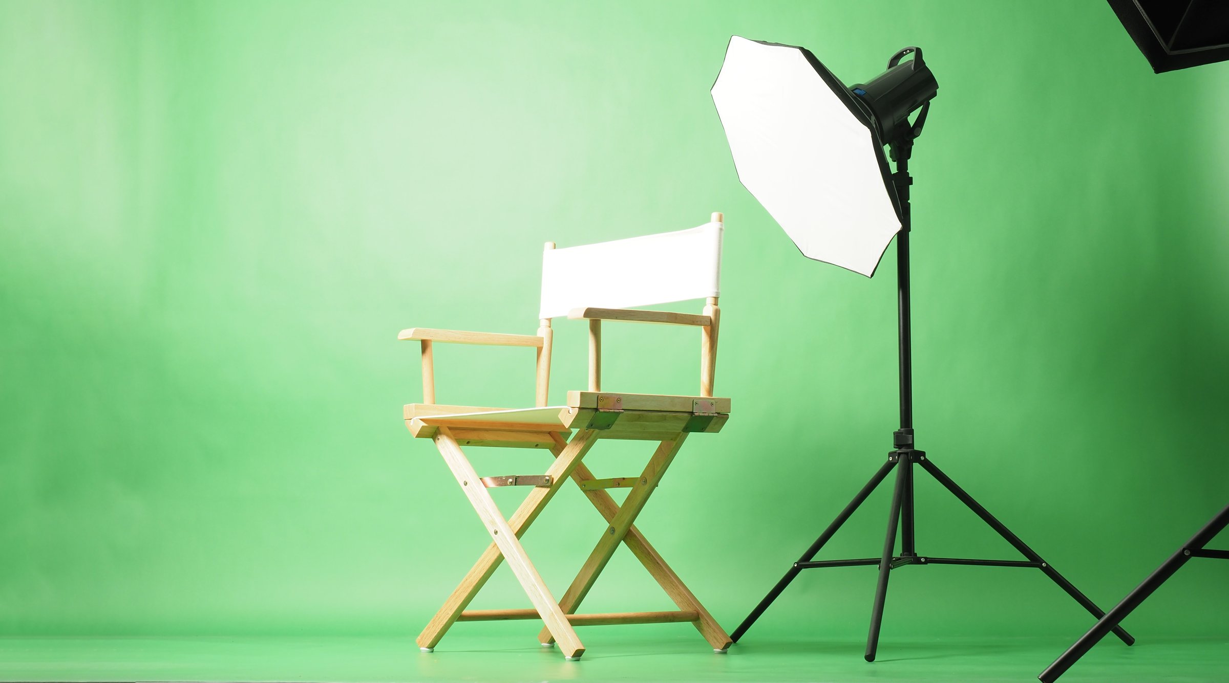 A director's chair and professional studio lighting setup in front of a green screen background.