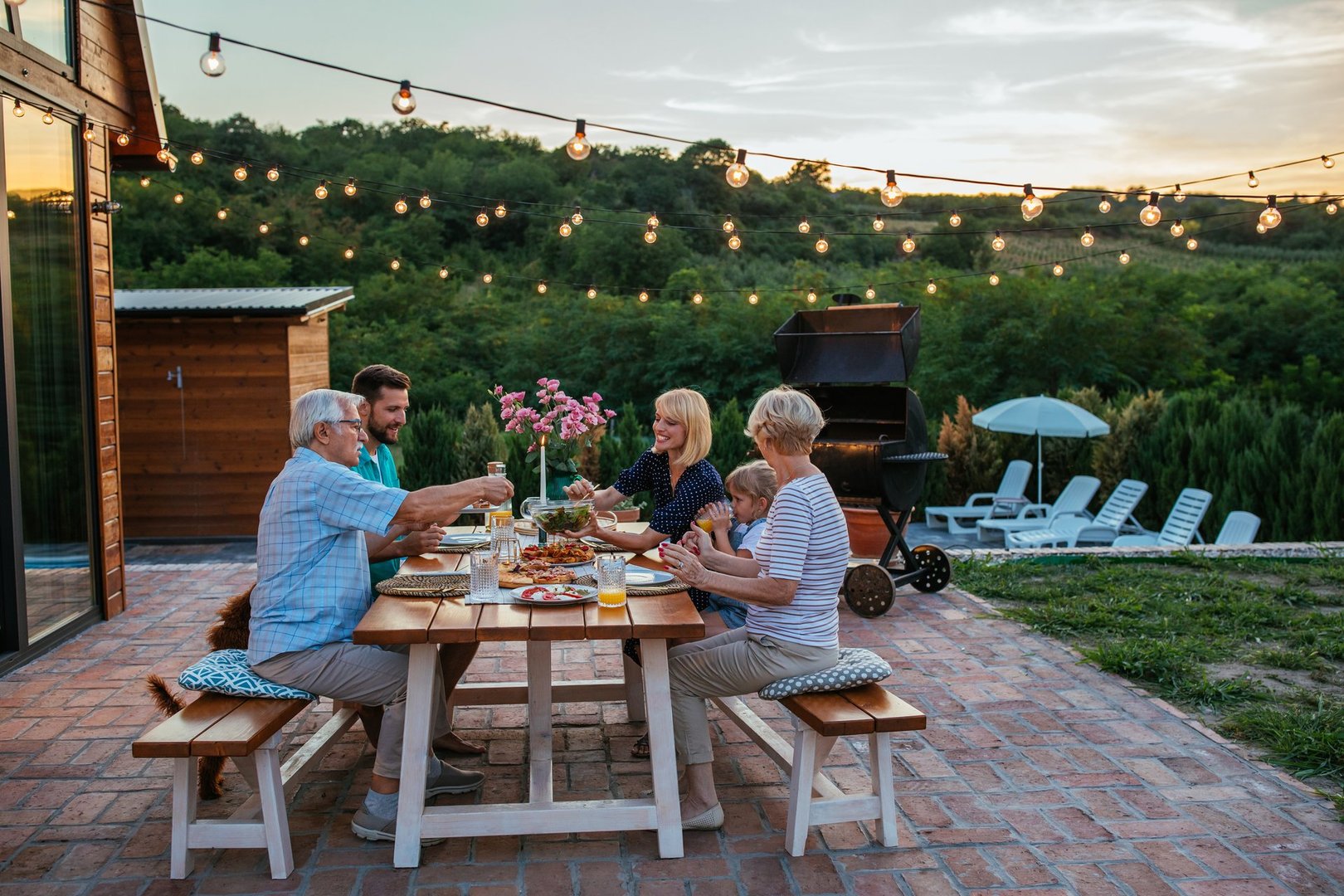 Happy family eating together outdoors. Smiling generation family sitting at dining table during dinner. Happy cheerful family enjoying meal together in garden.