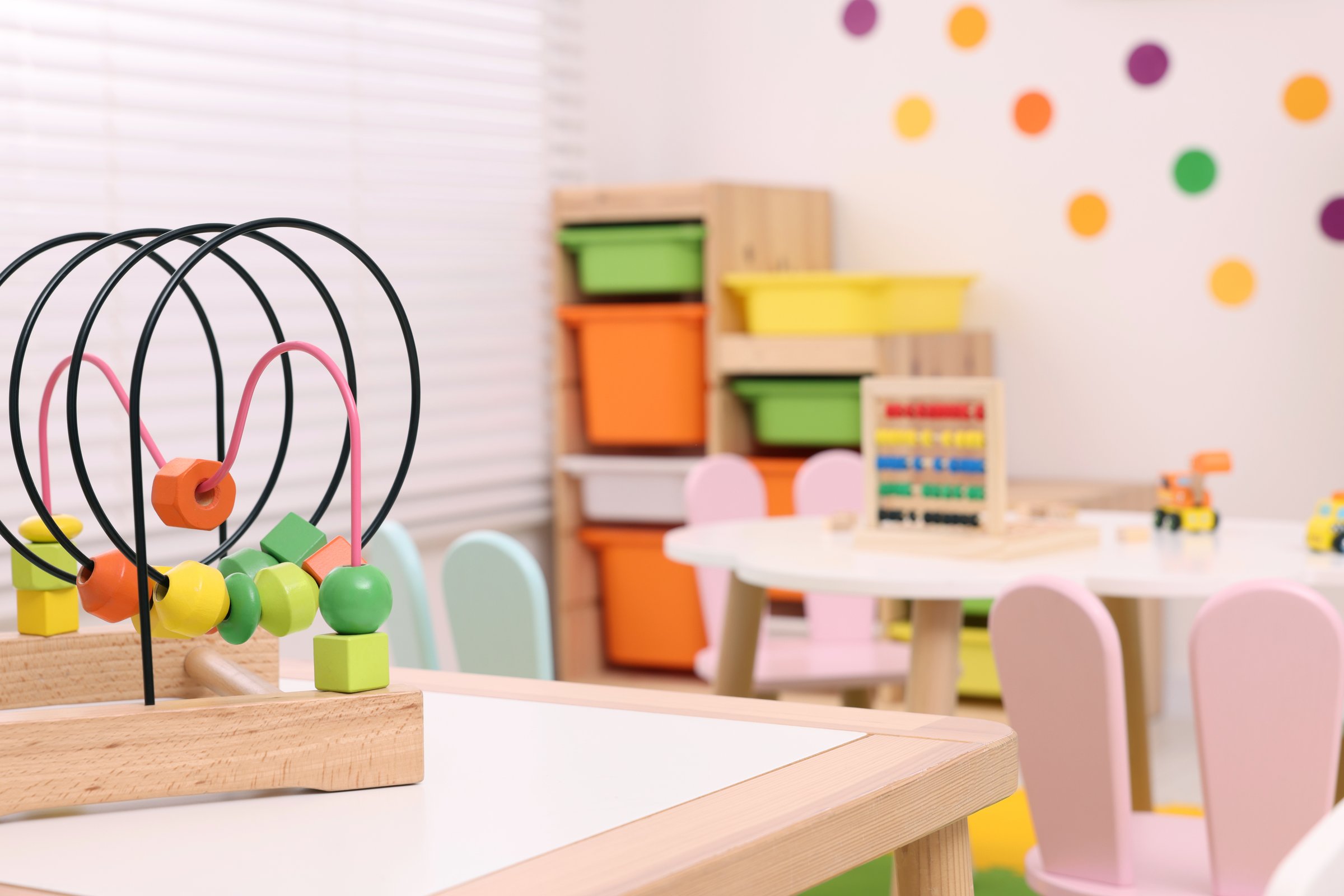 Toy bead maze on wooden table in playroom, space for text. Kindergarten interior design