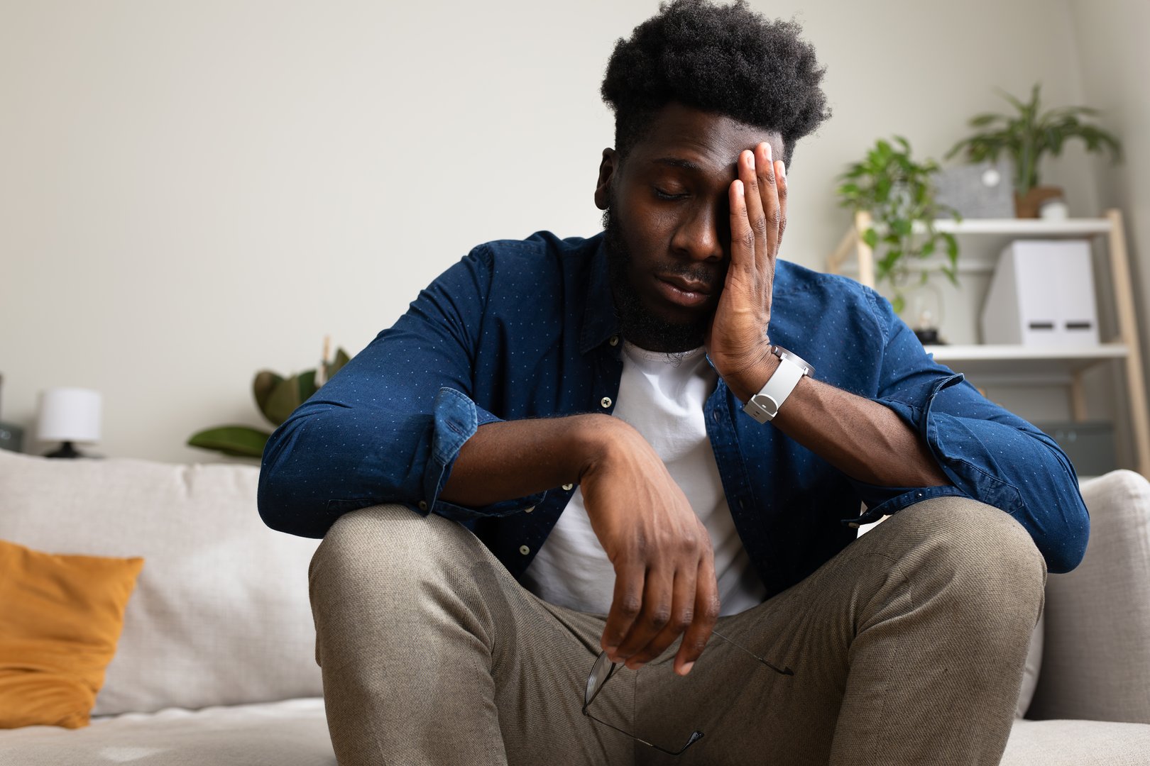 Overwhelmed African American man sitting on the couch, having anxiety and feeling sad. Depression and mental health concepts.