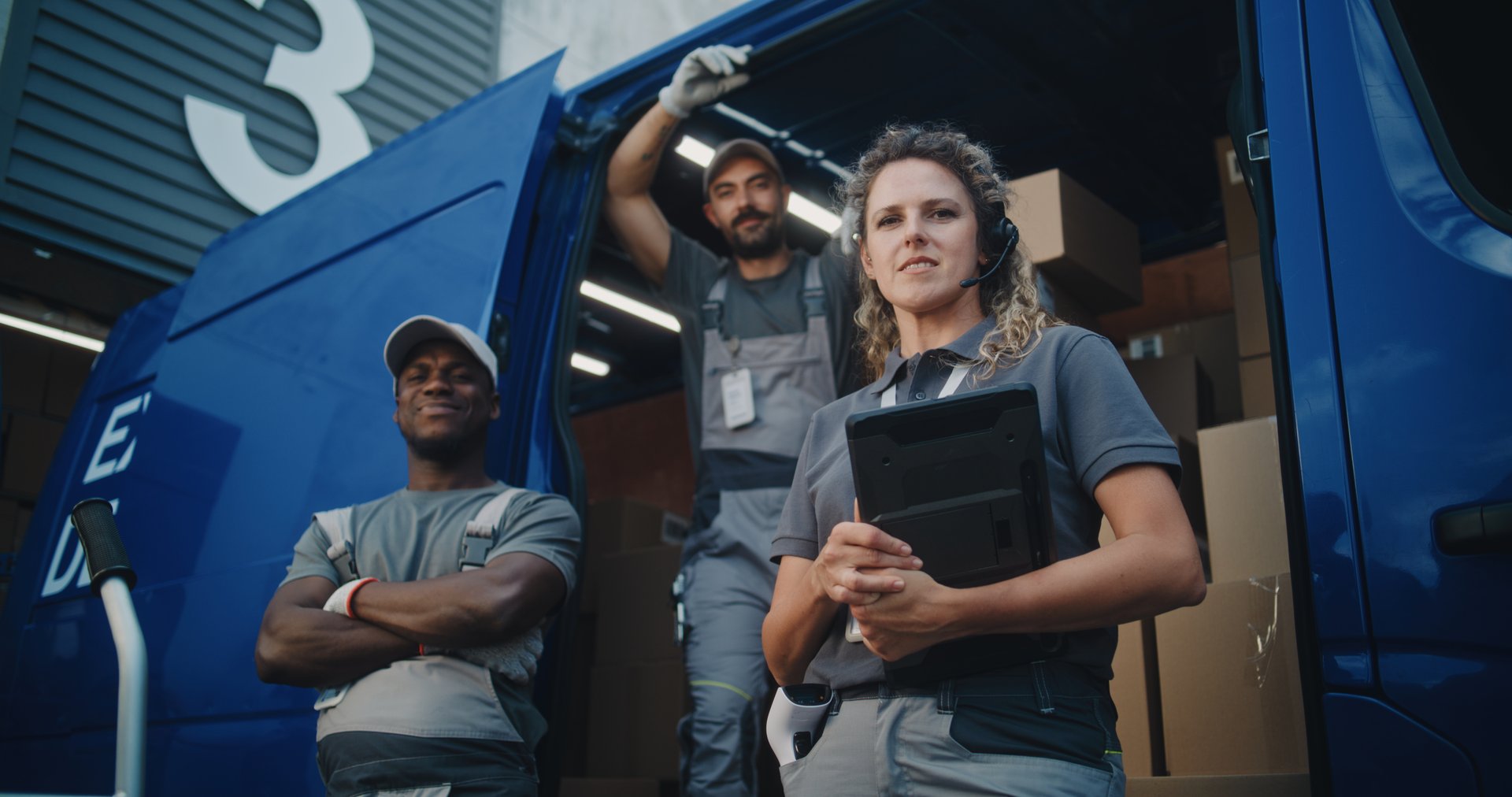 Outside of Logistics Distribution Warehouse: Team of Diverse Workers Standing near Delivery Truck Full of Cardboard Boxes with Online Orders, Looking at Camera. Female Manager Holding Digital Tablet.