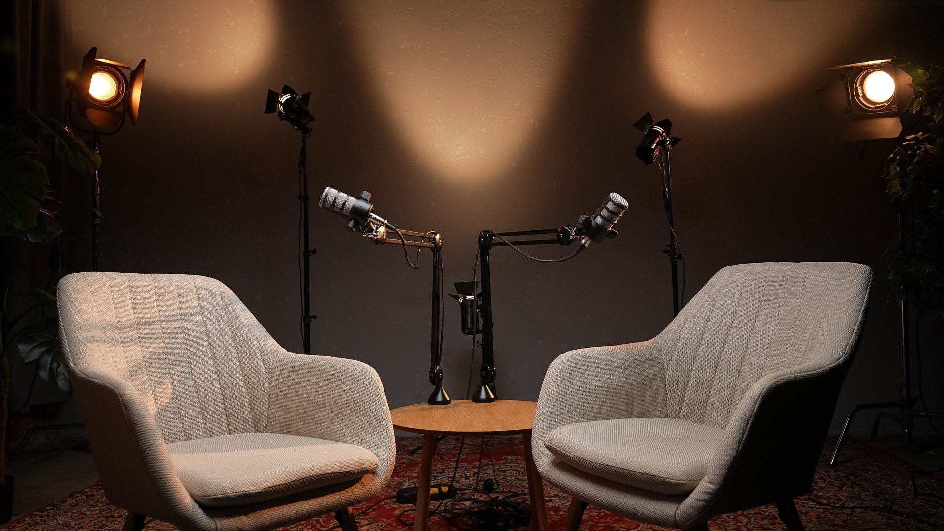 In a thoughtfully designed podcast studio, two stylish chairs face each other across a table, with microphones poised for an engaging interview. Soft light highlights the inviting space.