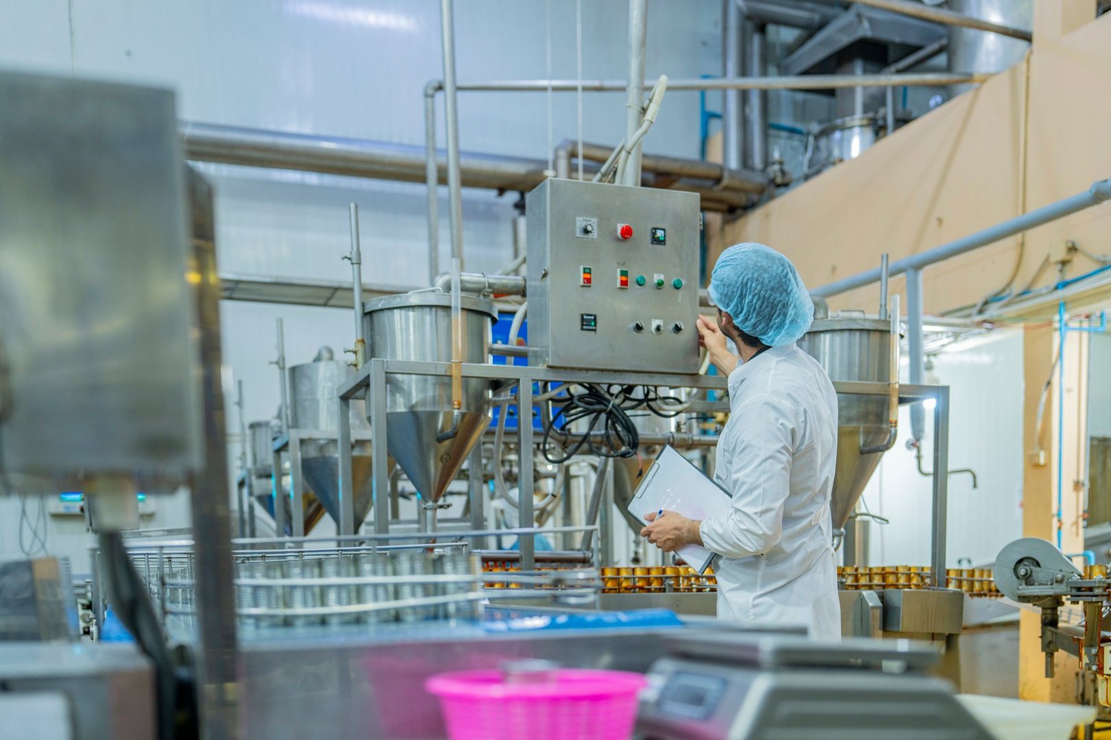 A professional factory worker inspects and monitors canned food processing on an automated assembly line in a modern industrial plant for quality assurance.