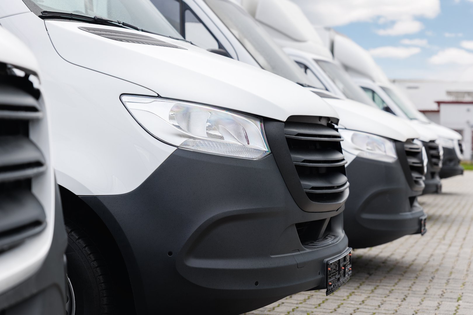 Fleet new modern electric hybrid hydrogen or diesel white vans parked in line row outdoors. Cargo freight industrial courier transportation logistics service. Commercial vehicle maintenance insurance.