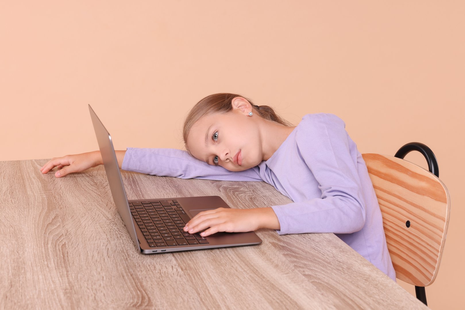 Girl with incorrect posture using laptop at wooden desk on beige background