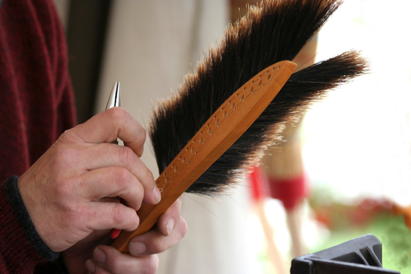 Person holding a shoe brush with wooden handle and dark bristles, performing shoe cleaning or maintenance.