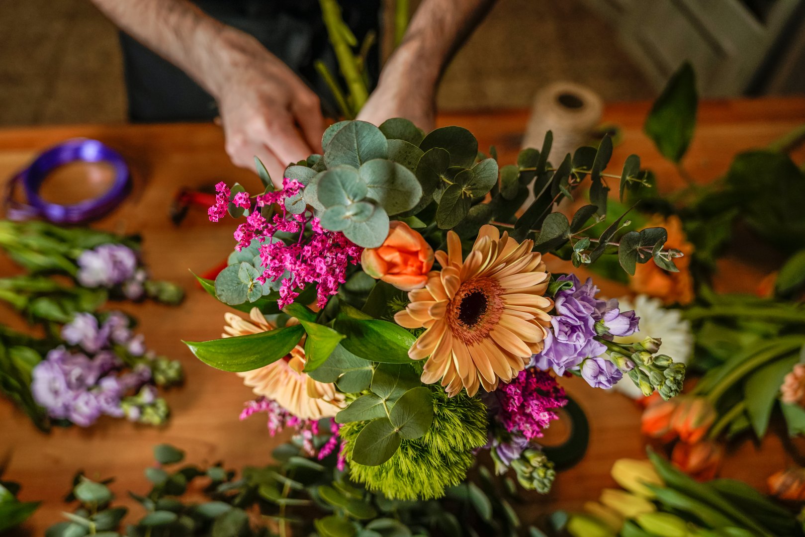 Florist creating a vibrant bouquet with gerbera daisies, eucalyptus, and various colorful flowers