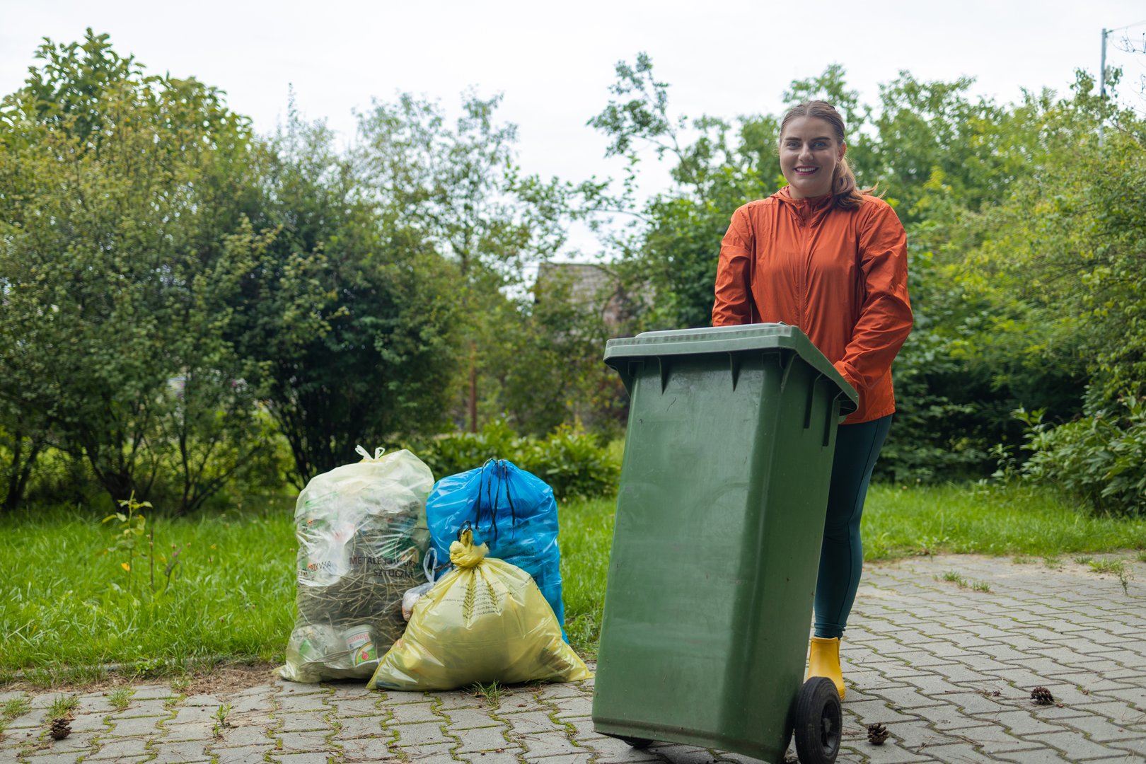 Adult happy 30s woman household taking out bin to the street on rubbish day. High quality photo