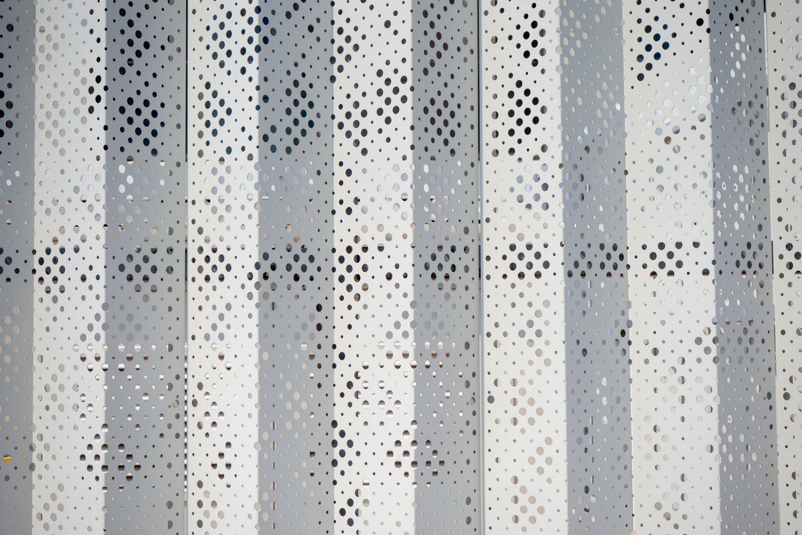 Decorative perforated metal facade panel with geometric patterns. Modern architectural exterior element. White metal protective cladding with laser-cut design for building facade