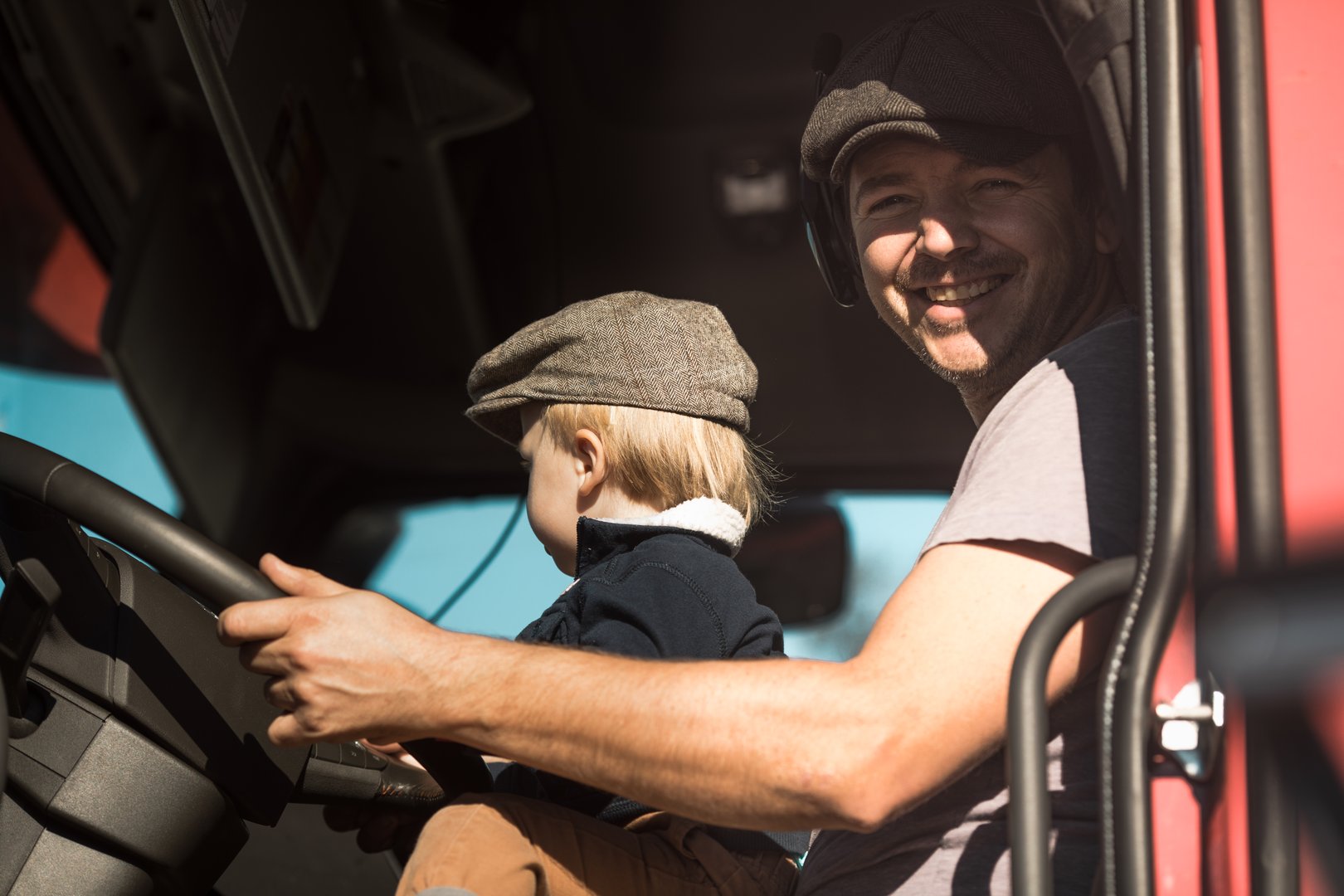 A Cute little boy driving is fathers truck with Dad