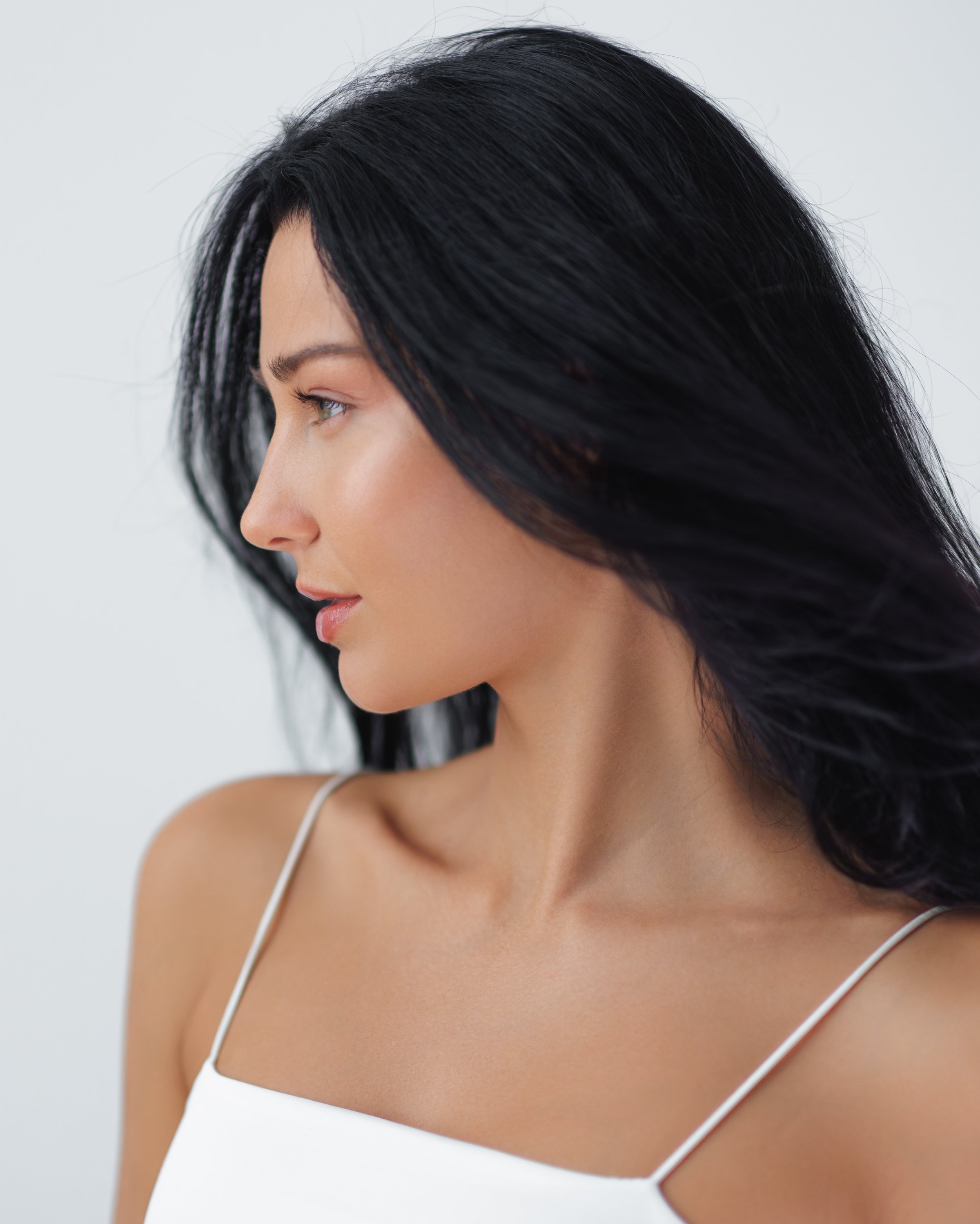 Profile portrait of a beautiful Japanese woman with dark, wind-swept hair and flawless skin. Ideal for hair care and skincare advertisements, capturing elegance and natural beauty in a studio setting.