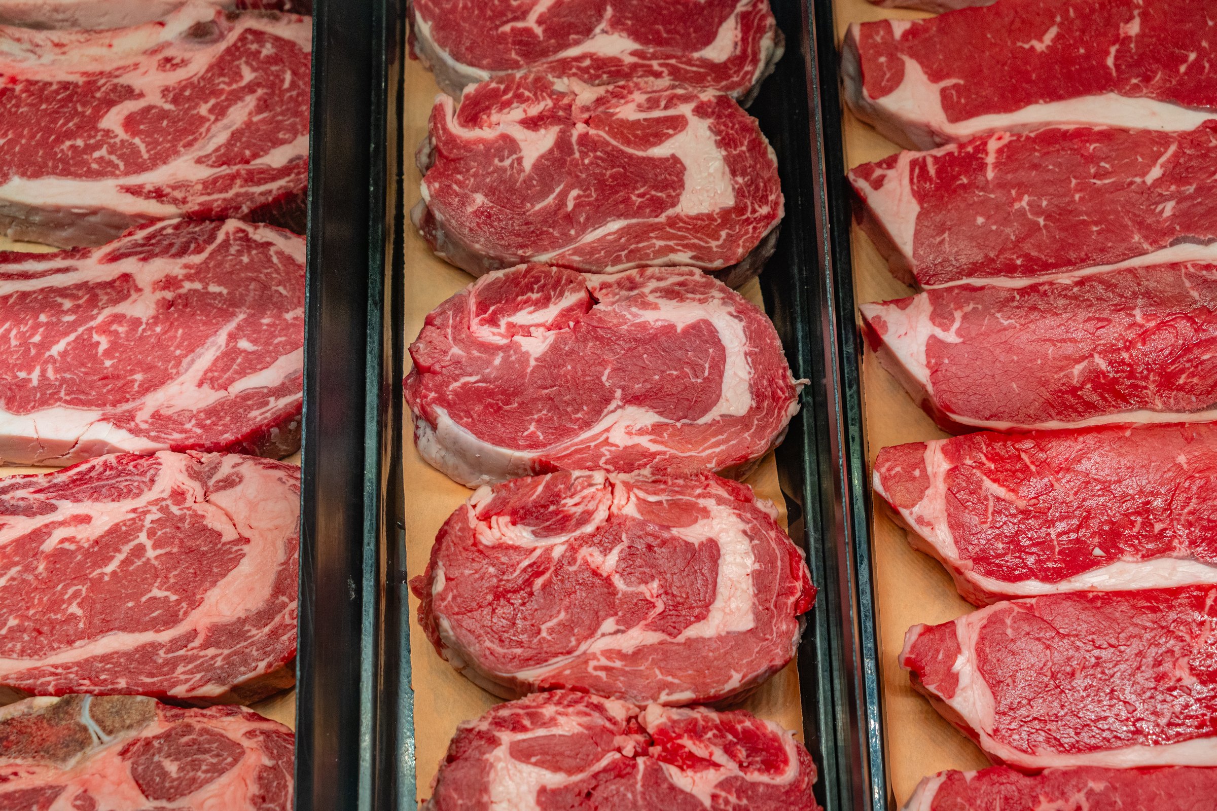 Various cuts of meat on display in grocery store refrigerator case.