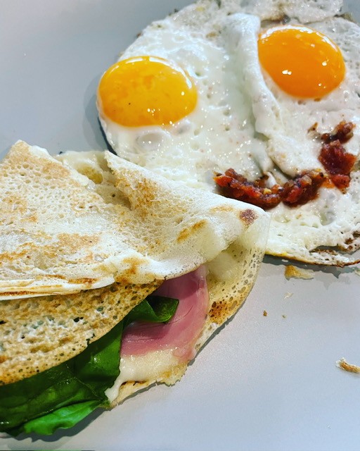 A crepe filled with spinach and ham beside two sunny-side-up eggs arranged to look like a smiling face.