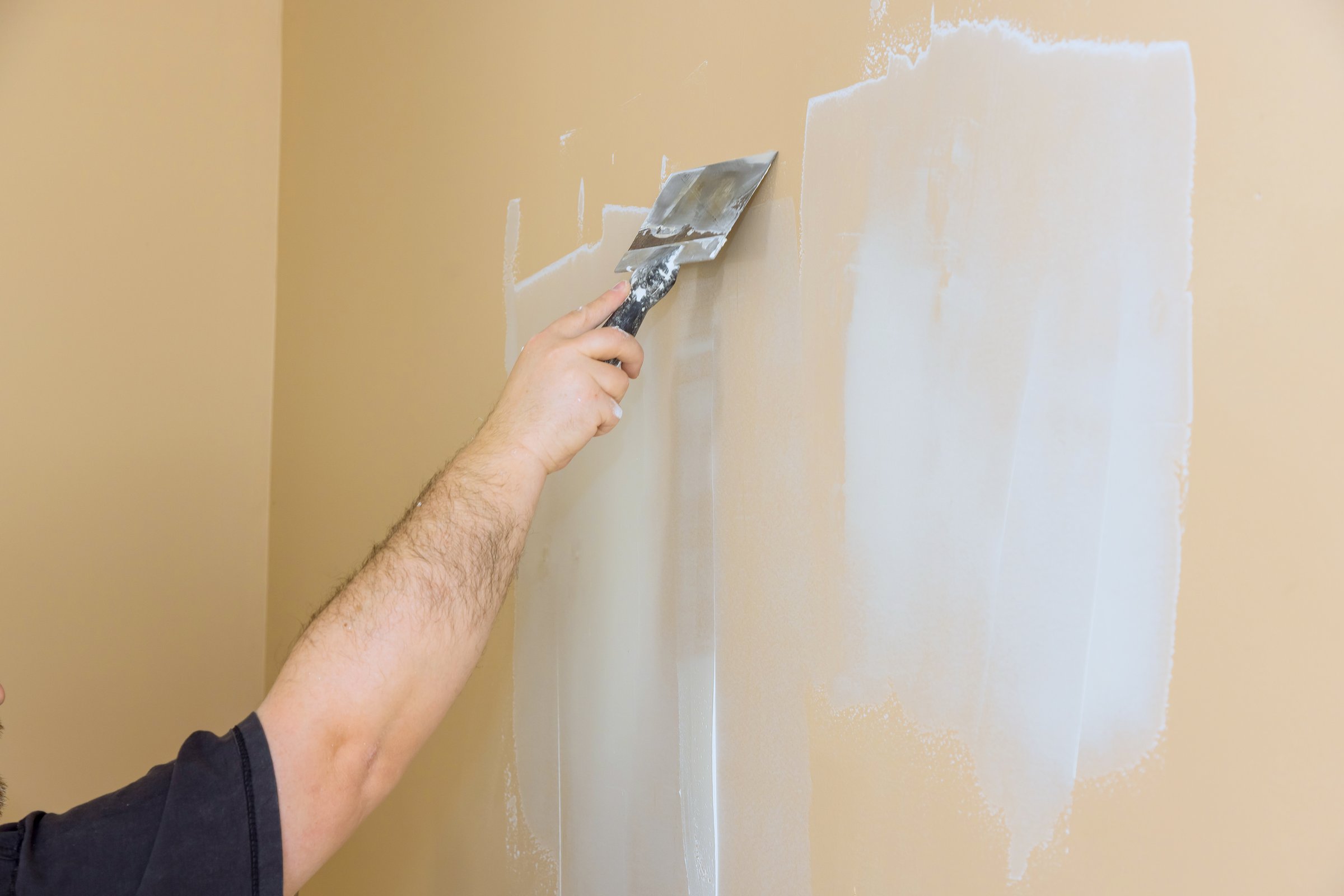 Worker is applying drywall compound to wall, preparing it for painting in residential living space.