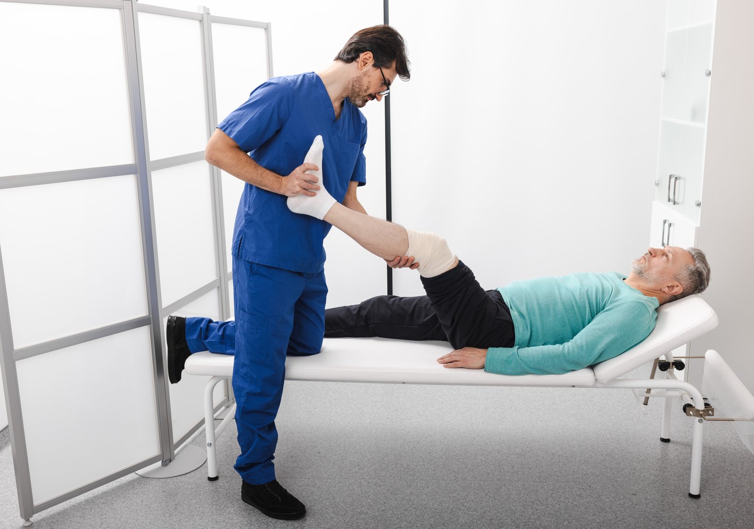 Healthcare professional conducts therapy on a patient's leg, focusing on rehabilitation for mobility improvement in a clinical environment