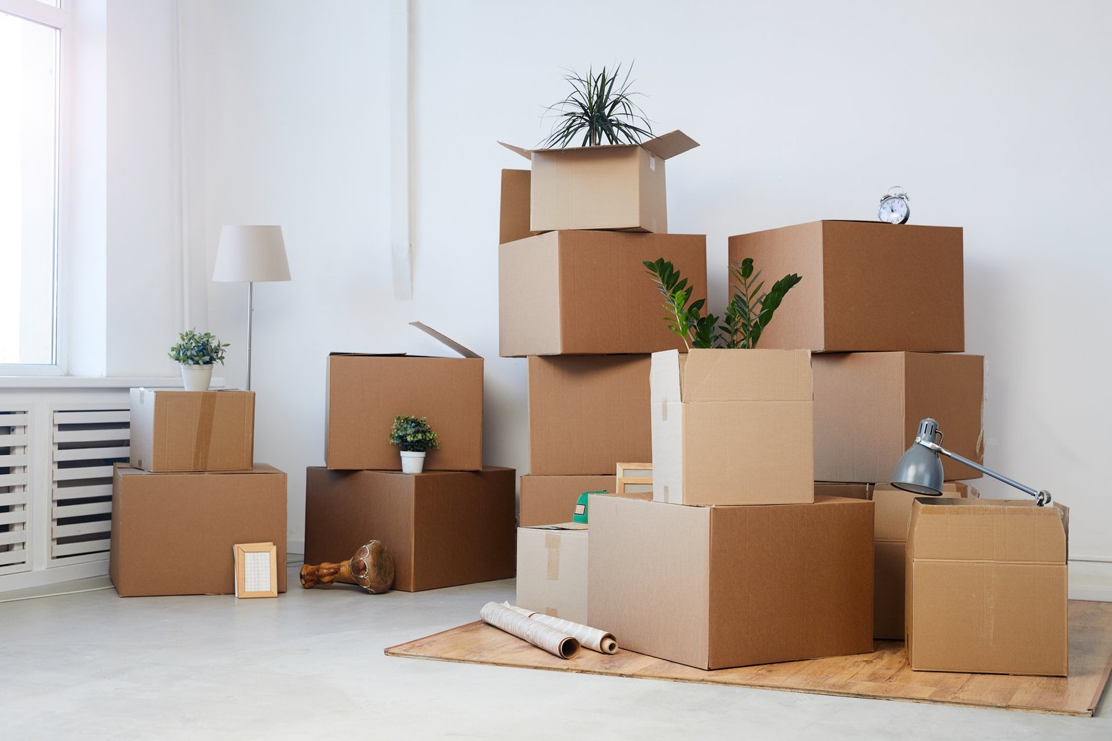 Minimal background image of cardboard boxes stacked in empty room with plants and personal belongings inside, moving or relocation concept, copy space