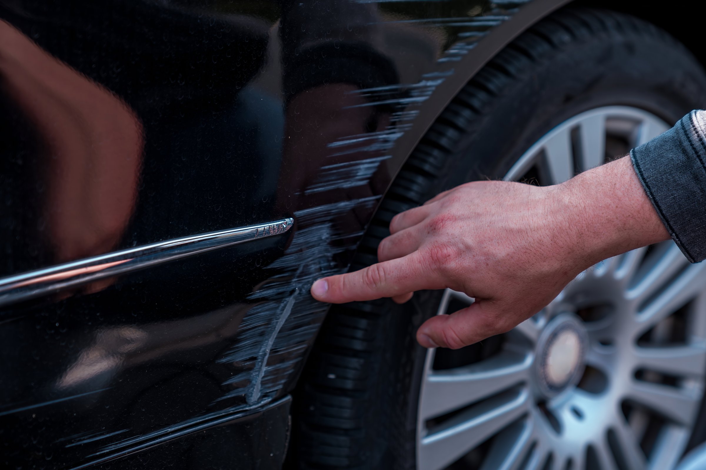 Man examining a scratch on black car side panel