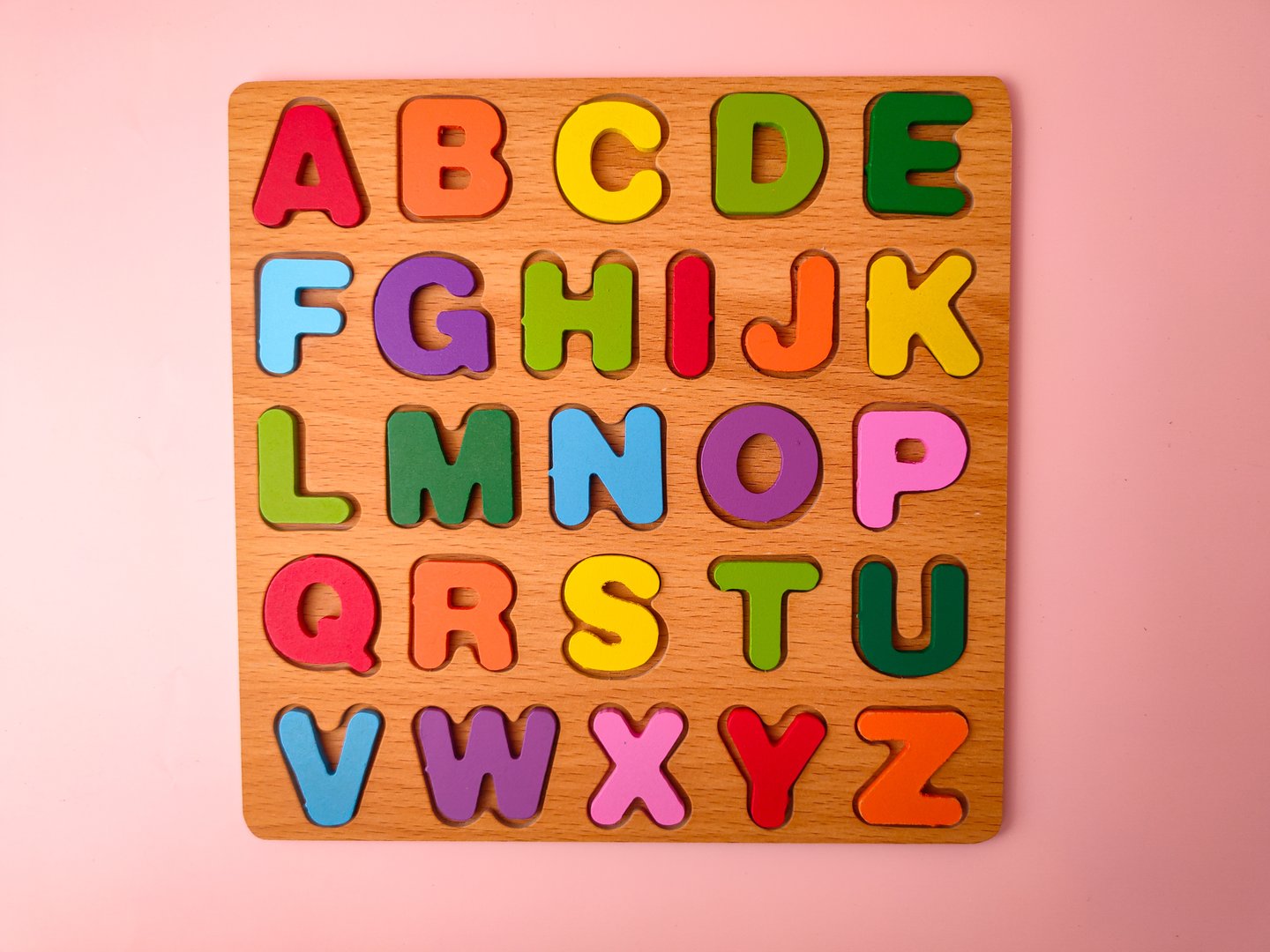 This item is a wooden alphabet puzzle board on a pink background.