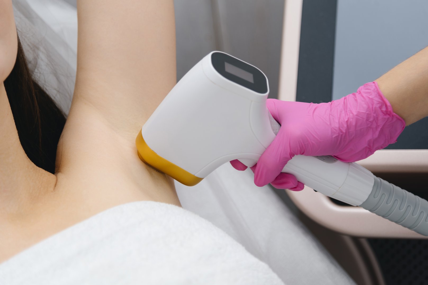 laser epilation, hair removal procedure, young beautiful caucasian smiling brunette woman lying on couch in beauty salon, armpits epilation, pink gloves, spa and cosmetology concept