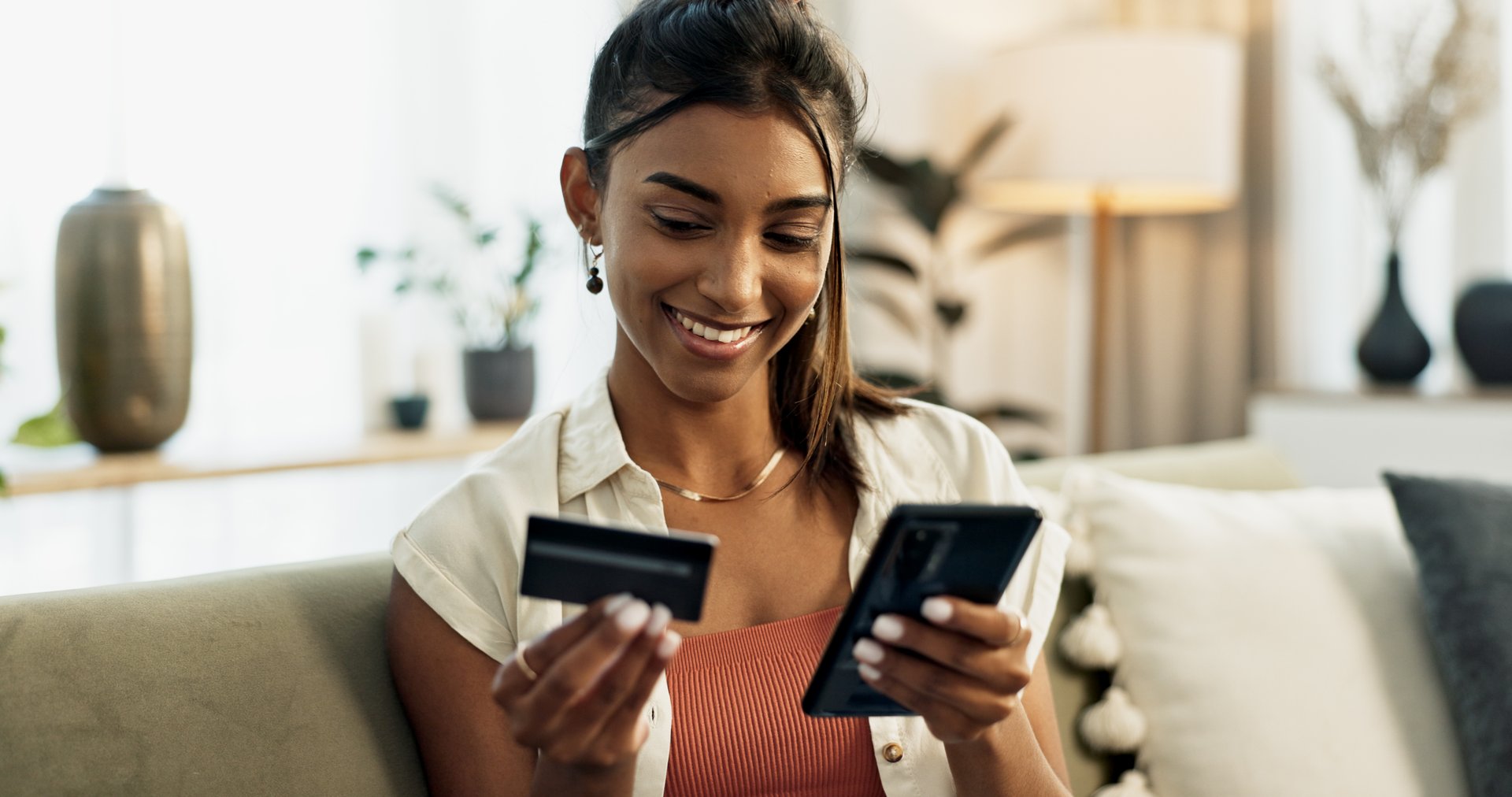Woman, credit card and phone on sofa, smile or reading with cybersecurity, fintech app or bank info in home. Girl, smartphone and payment for password, budget or online shopping on e commerce website