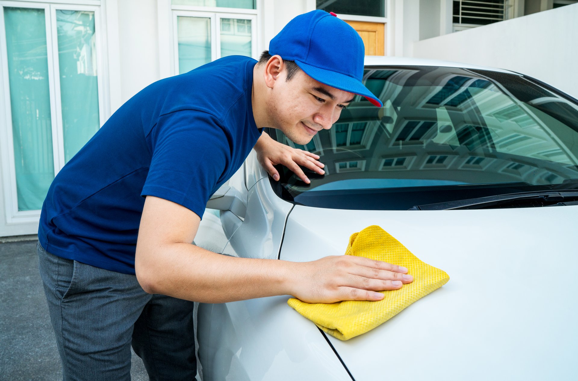 Car detailing, Man in blue uniform clean a white car in hand holding a microfiber washing large car