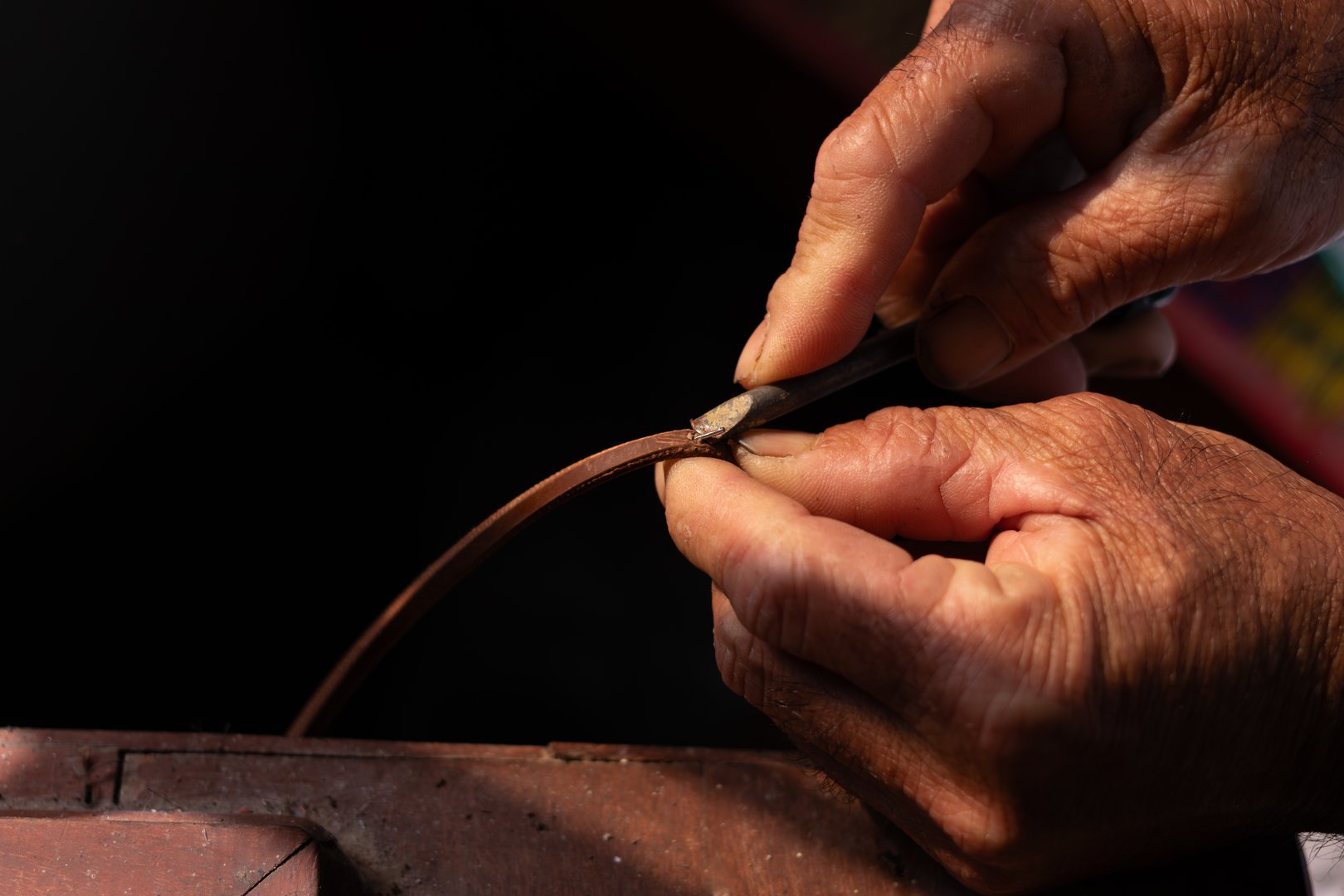 African American artisan meticulously cutting and beveling leather strap edge on wooden workbench