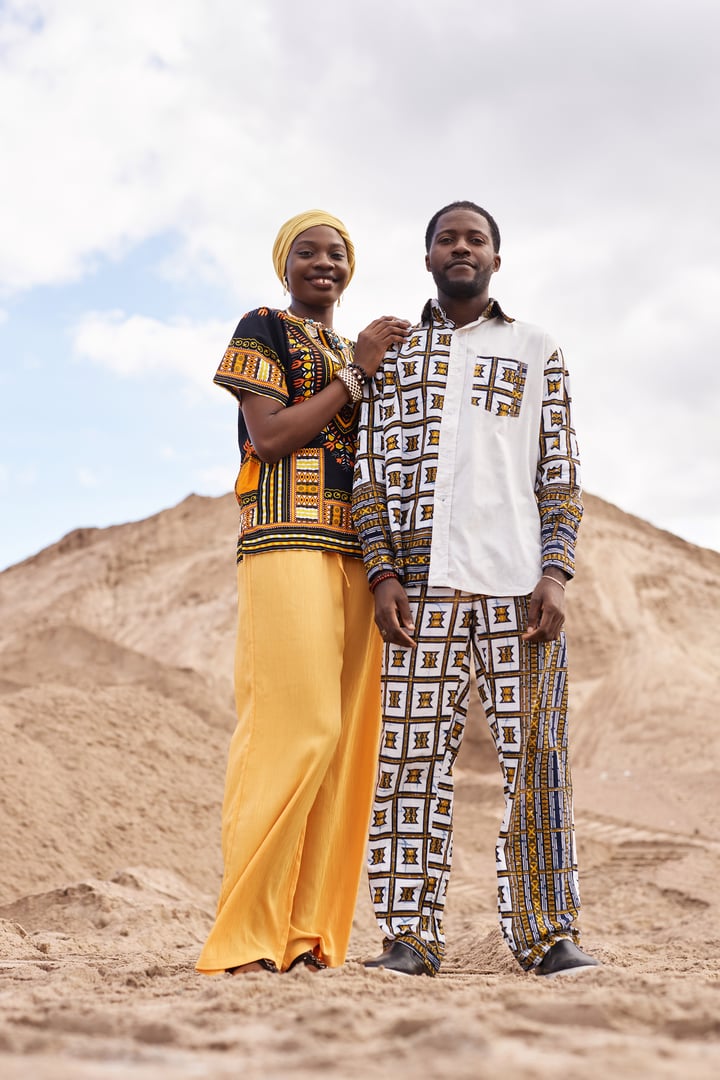 Vertical full length portrait of young Black couple wearing traditional clothing posing in desert landscape and looking at camera