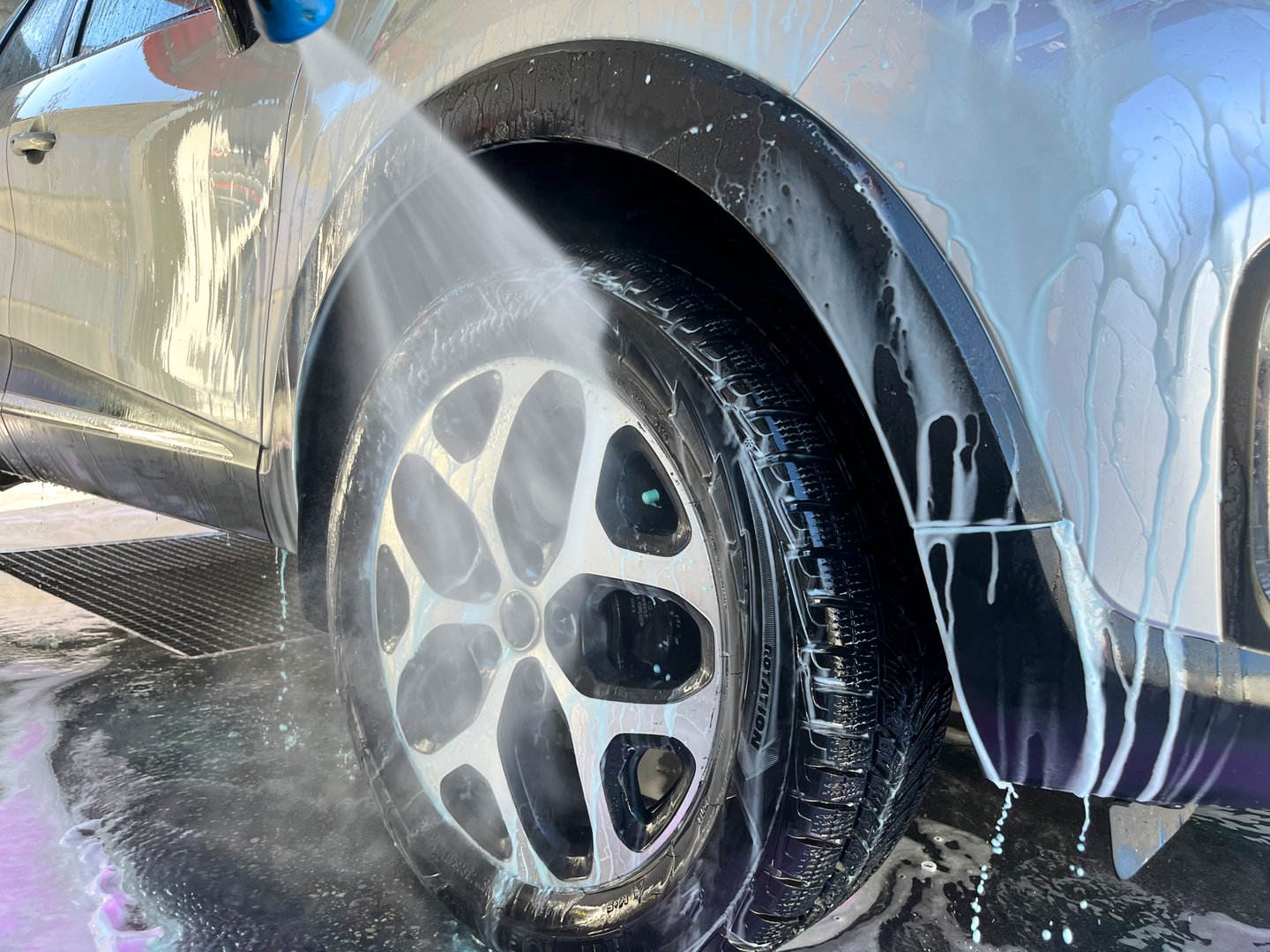 A silver car at a car wash after cleaning with active foam, wax is applied.