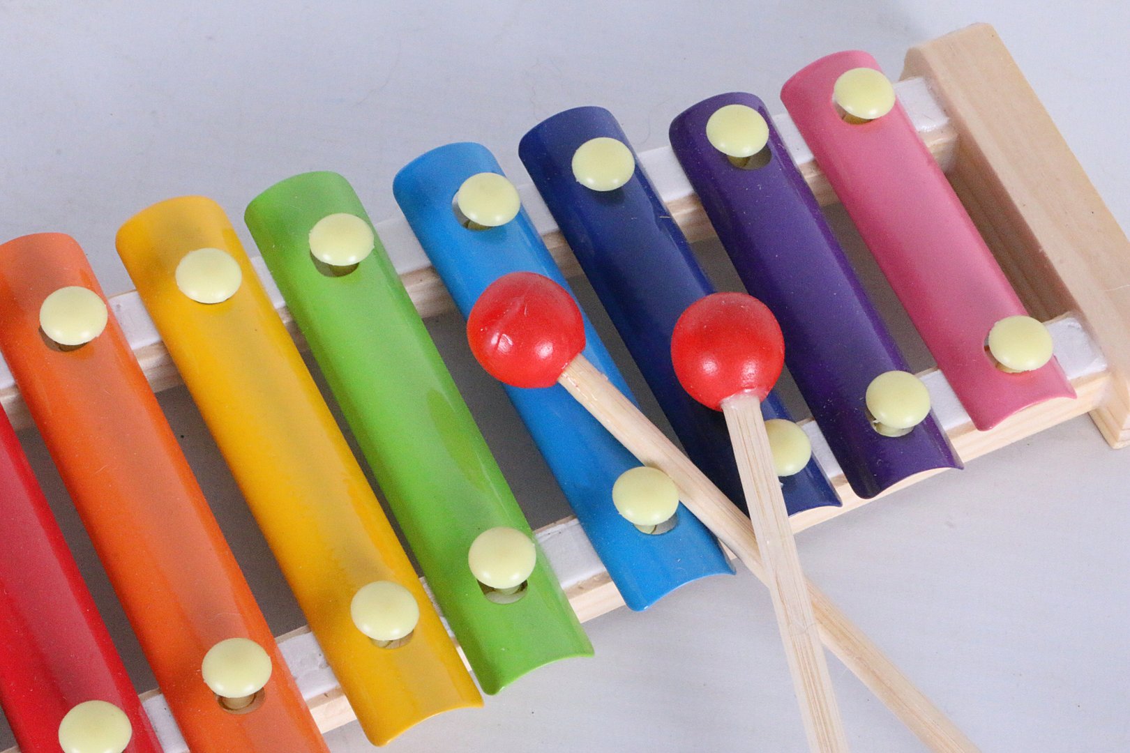 small wooden xylophone with colorful keys and 2 mallets with red balls lying on a white background
