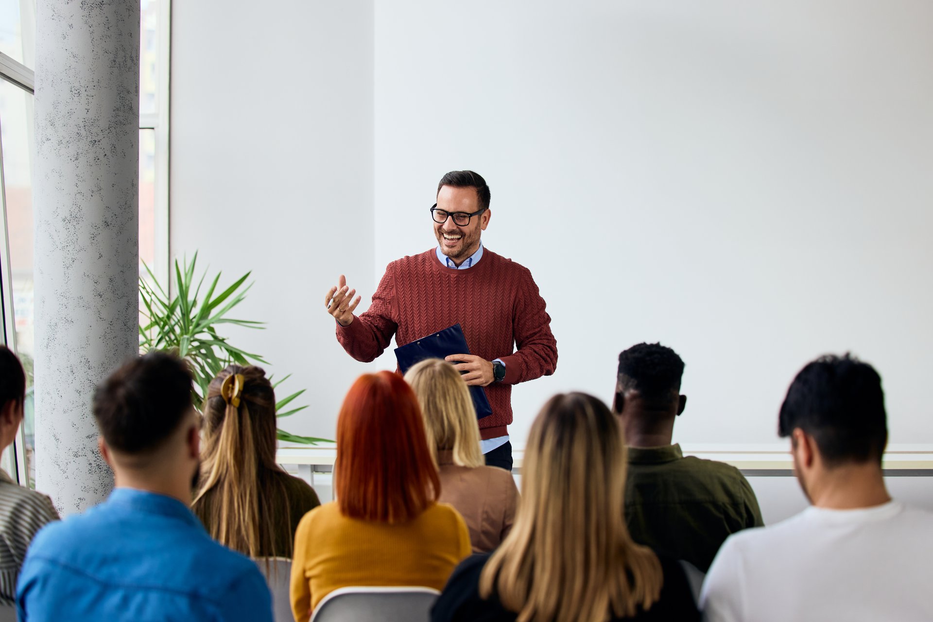 A cheerful instructor delivering a speech to a multicultural audience in a bright room.