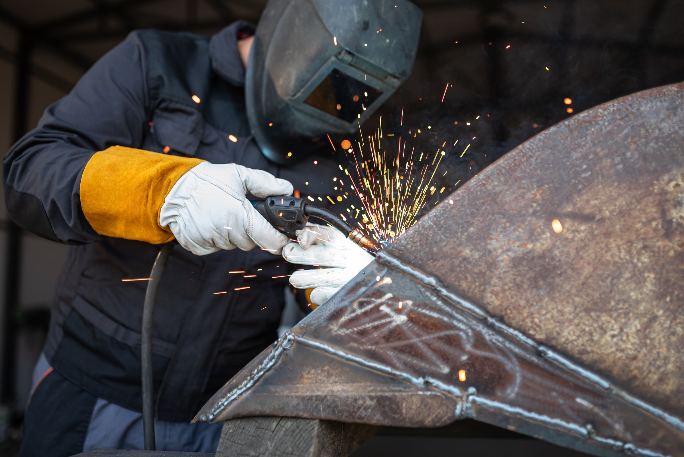 Welder wearing protective gear and using a mig mag welding torch is joining metal parts, creating a shower of sparks