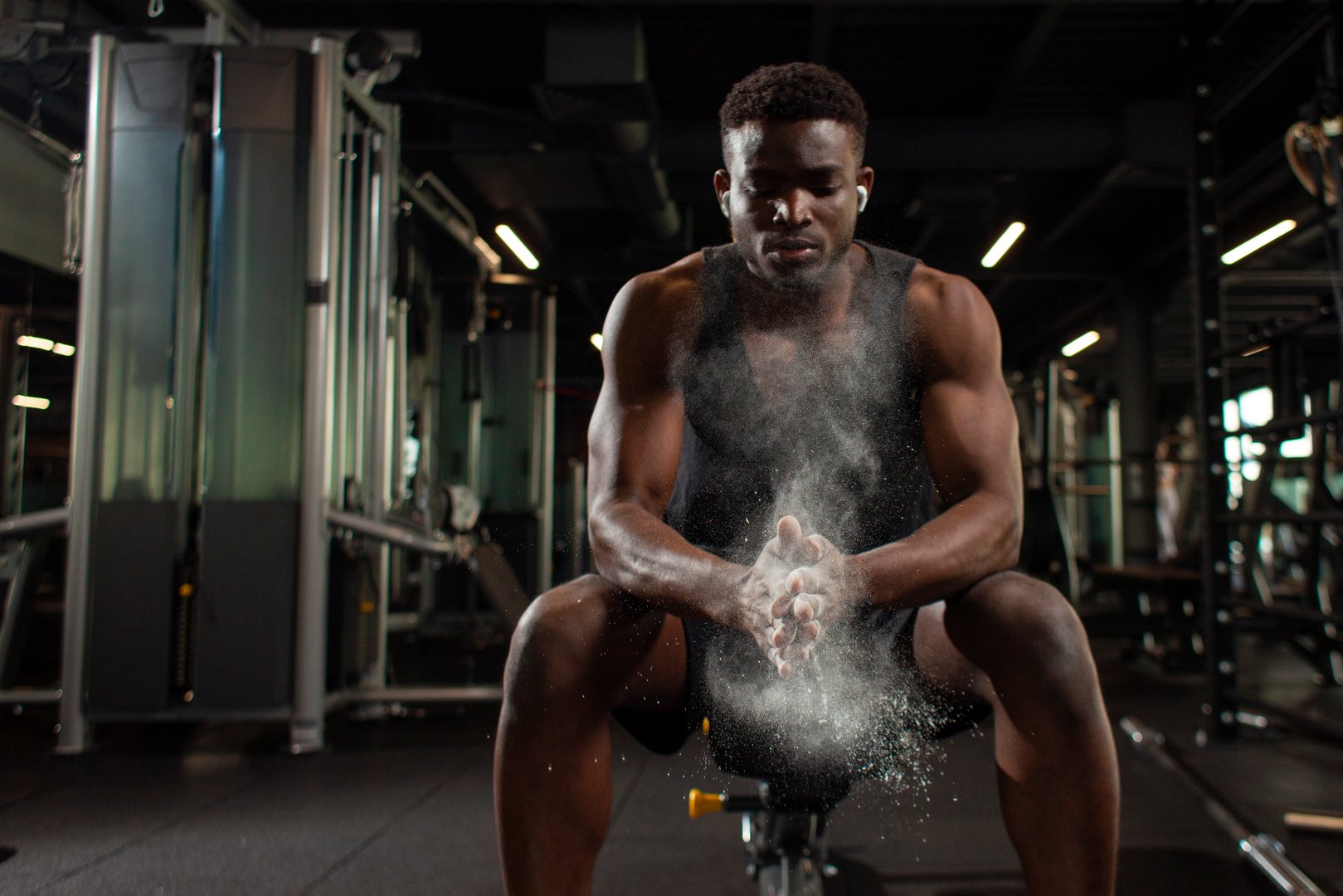 sporty african american man trains in dark gym and rubs his hands with magnesia, young guy makes clap with his hands in the fitness room, close-up of dust and flour with the hands of athlete