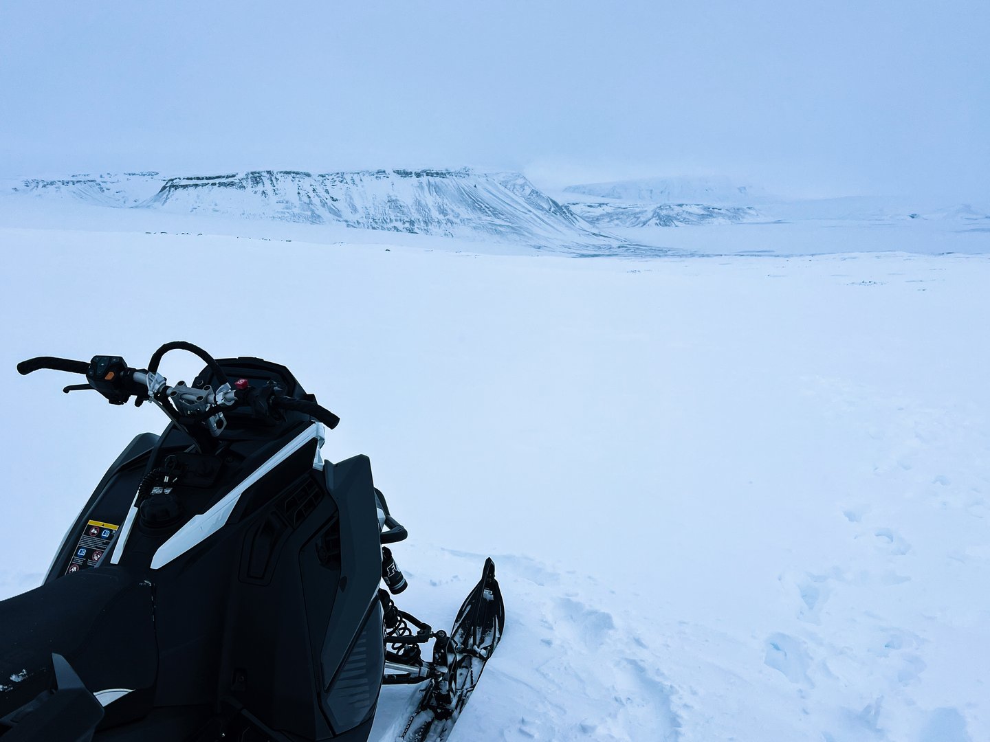 A snowmobile parked against a stunning backdrop of snowy mountains. Clear skies and untouched snow emphasize the thrill of winter exploration in high altitudes.