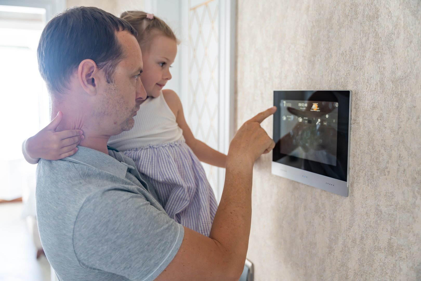 Daughter in her father using tablet panel application for control smart home living. Wireless device controller for home automation IoT on the wall. High quality photo
