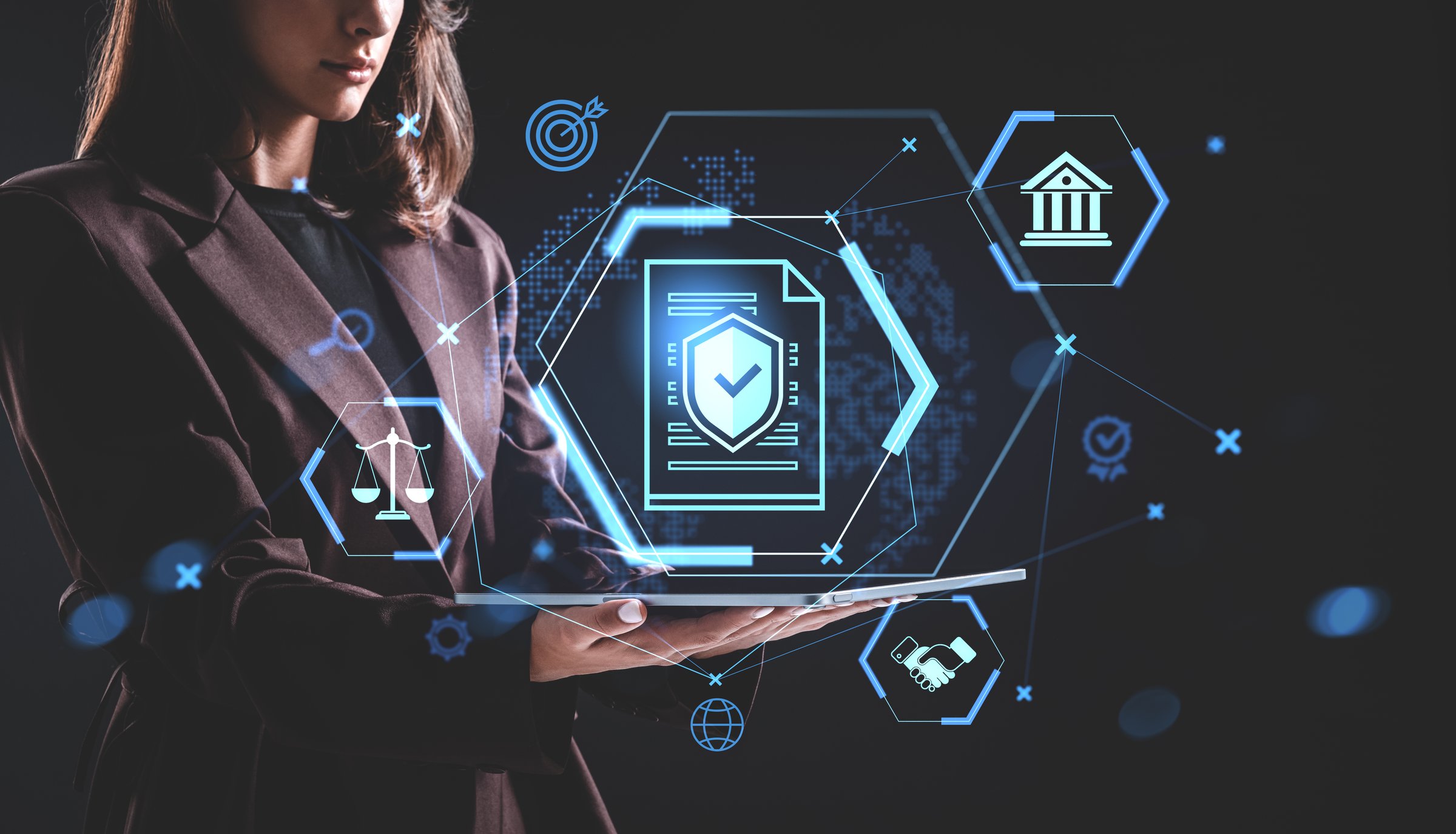 Woman in suit holds tablet with glowing hologram icons of law and security on dark background, illustrating legal technology and digital compliance concept