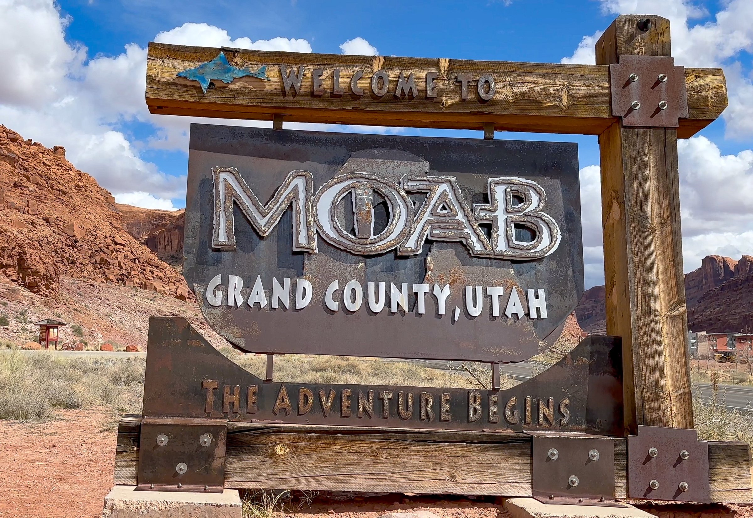 A welcome sign to Moab, Utah with red rock cliffs in the background. The Adventure Begins is written on the sign, inviting visitors to explore the area and all that it has to offer - USA
