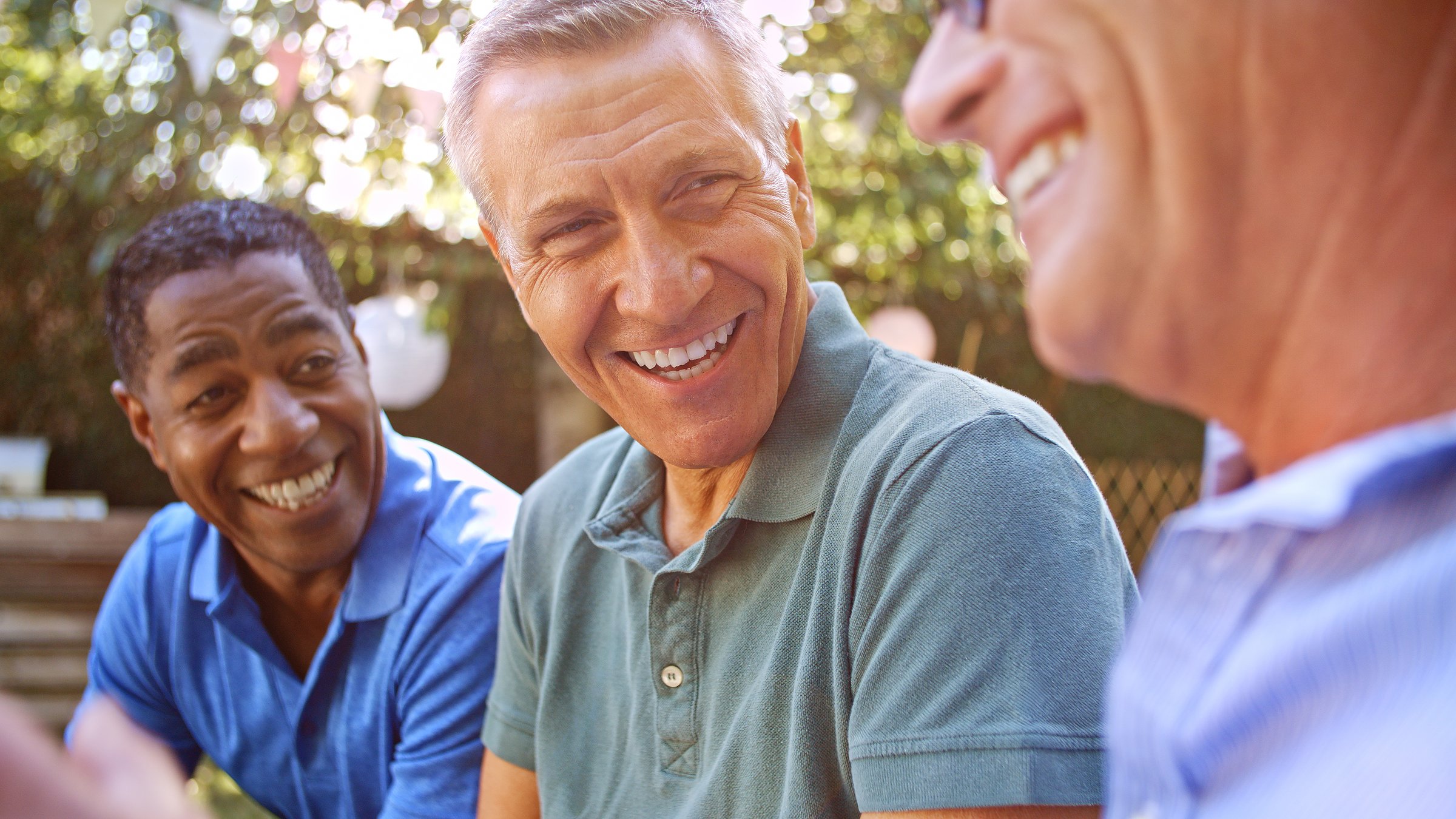 Close Up Of Smiling Mature Male Friends Socializing In Backyard Together