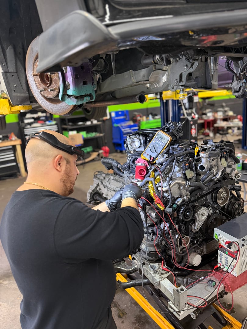 Two mechanics working together to diagnose car issue using laptop in repair garage. Teamwork and technology in automotive service.