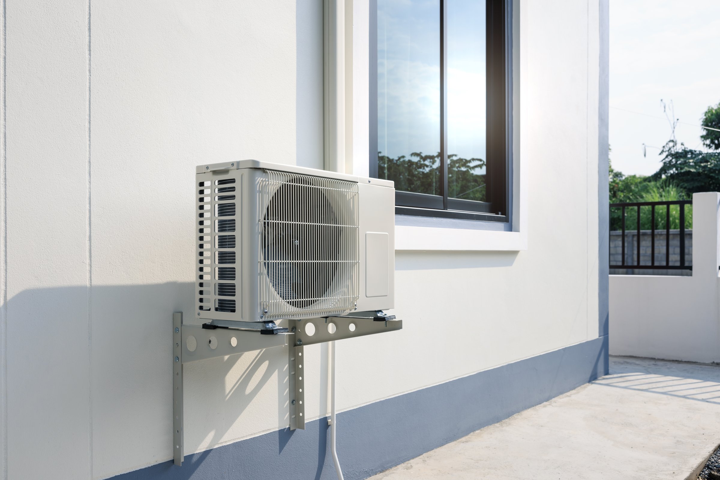 Condenser unit or compressor outside home or residential building. Unit of central air conditioner AC or heating ventilation air conditioning system HVAC. Electric fan and refrigerant pump inside.