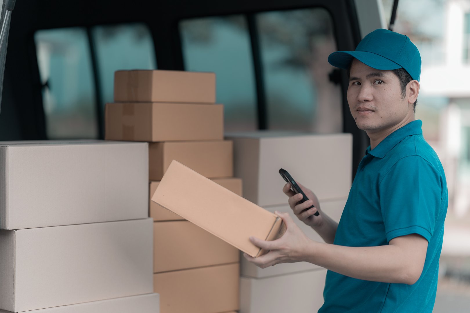 Asian male courier standing in front of house holding yellow box, delivery concept